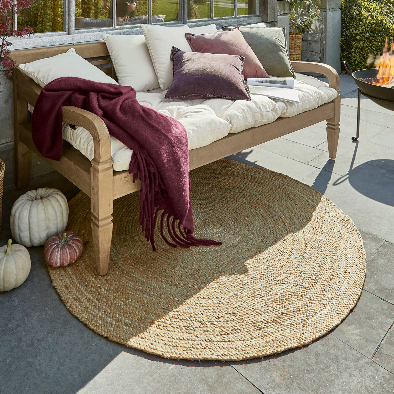 Teppich Imene Runder Jute-Teppich in Naturfarbe unter einer Holzbank mit Kissen und bordeauxroter Decke