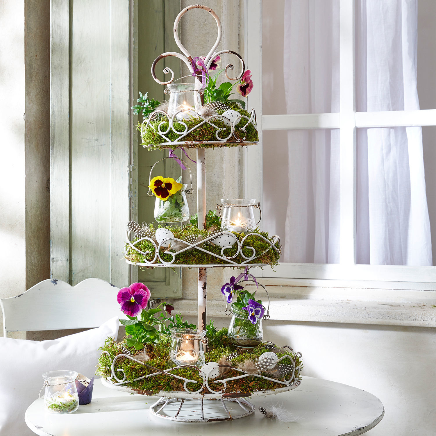 Etagere Julye Dreistöckiges weißes Metall-Etagere mit Moos, Blumen und Kerzen als Dekoration auf weißem Tisch