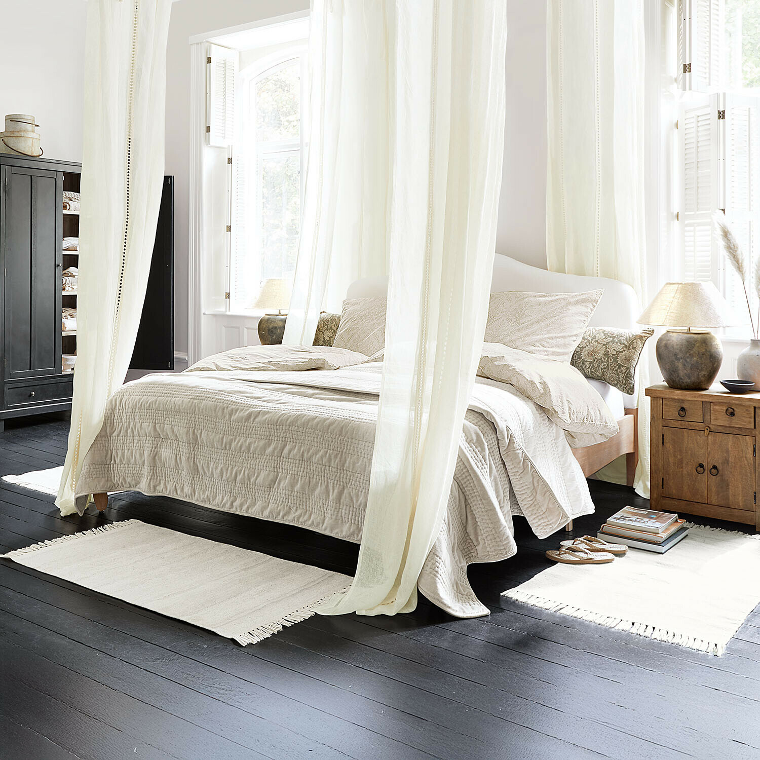 Gemütliches Schlafzimmer mit hellem Bettzeug und Holz-Nachttisch auf dunklem Boden