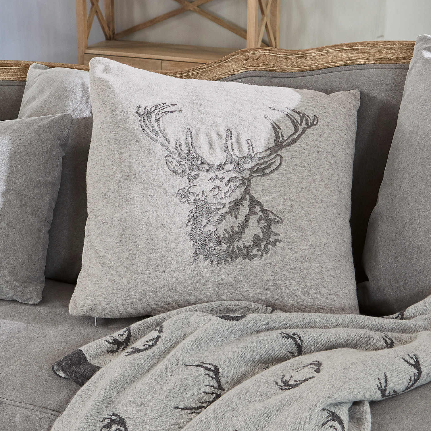 Kissenhülle Dario Graues Kissen aus weichem Material mit Hirschmotiv auf grauem Sofa mit passender Hirschdecke