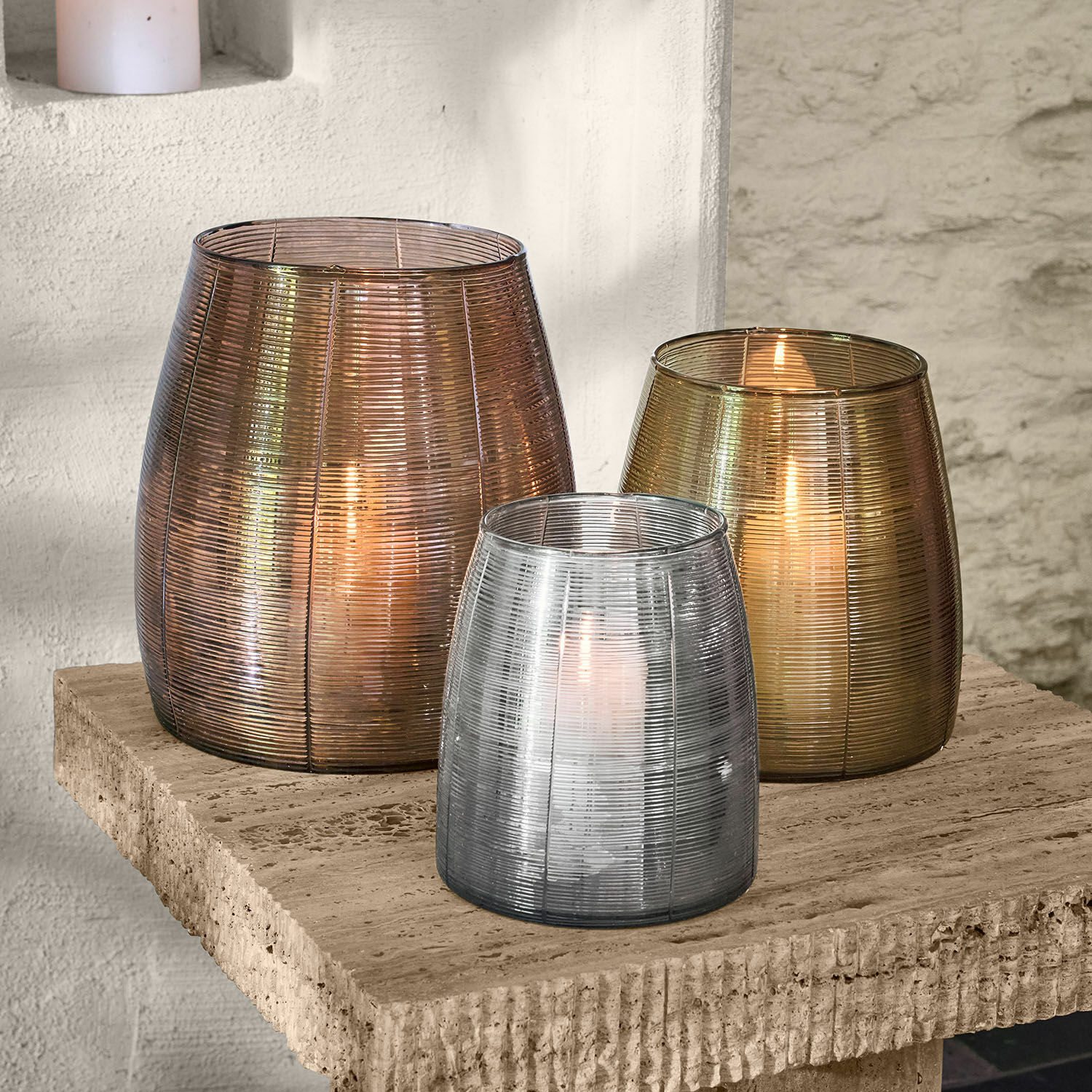 Drei Glaslaternen in Bronze-, Gold- und Silberfarben auf einem Steintisch dekorativ arrangiert