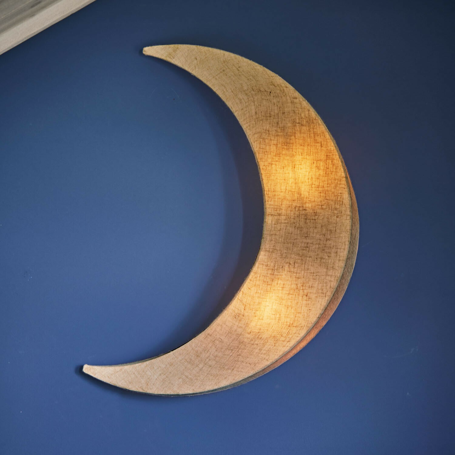 Wandlampe Jollymoon Wandlampe in Mondform aus beigem Stoff vor blauem Hintergrund