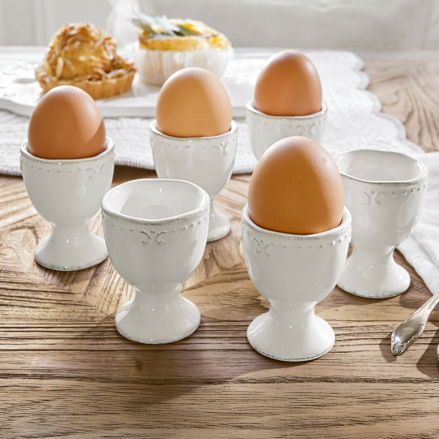 Eierbecher 6er Set Fontienne Set aus weißen Keramik-Eierbechern mit braunen Eiern auf hellem Holztisch