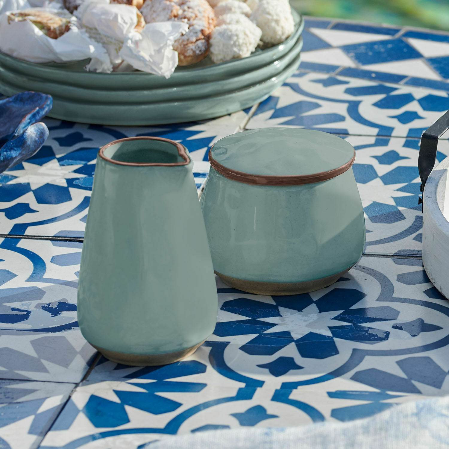 Grüner Keramikkrug und Dose auf blau-weiß gemustertem Tisch