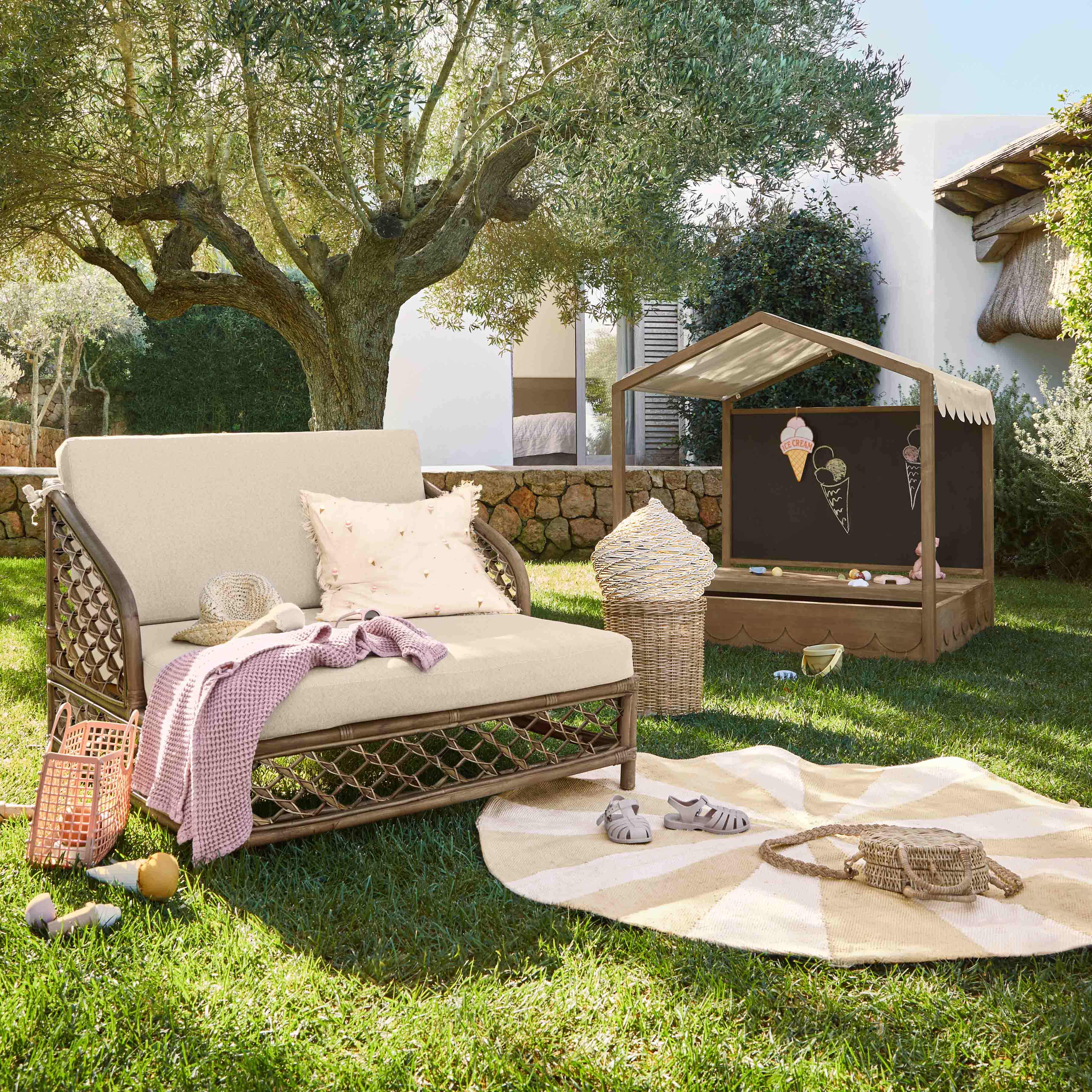 Garten mit beige Liegestuhl, Kissen und rosa Decke auf Gras unter einem Olivenbaum