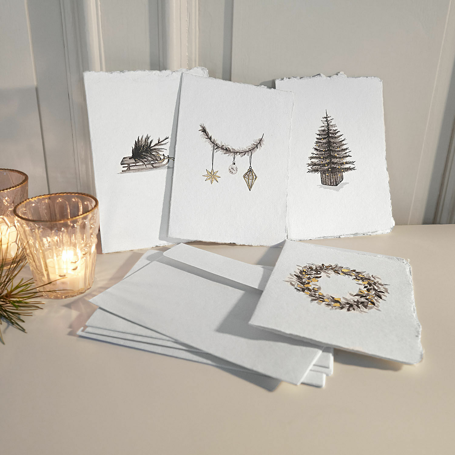 Geschenkkarte 4er Set Aelindor Set aus weißen Karten mit Weihnachtsmotiven und Umschlägen auf hellem Untergrund mit Windlichtern