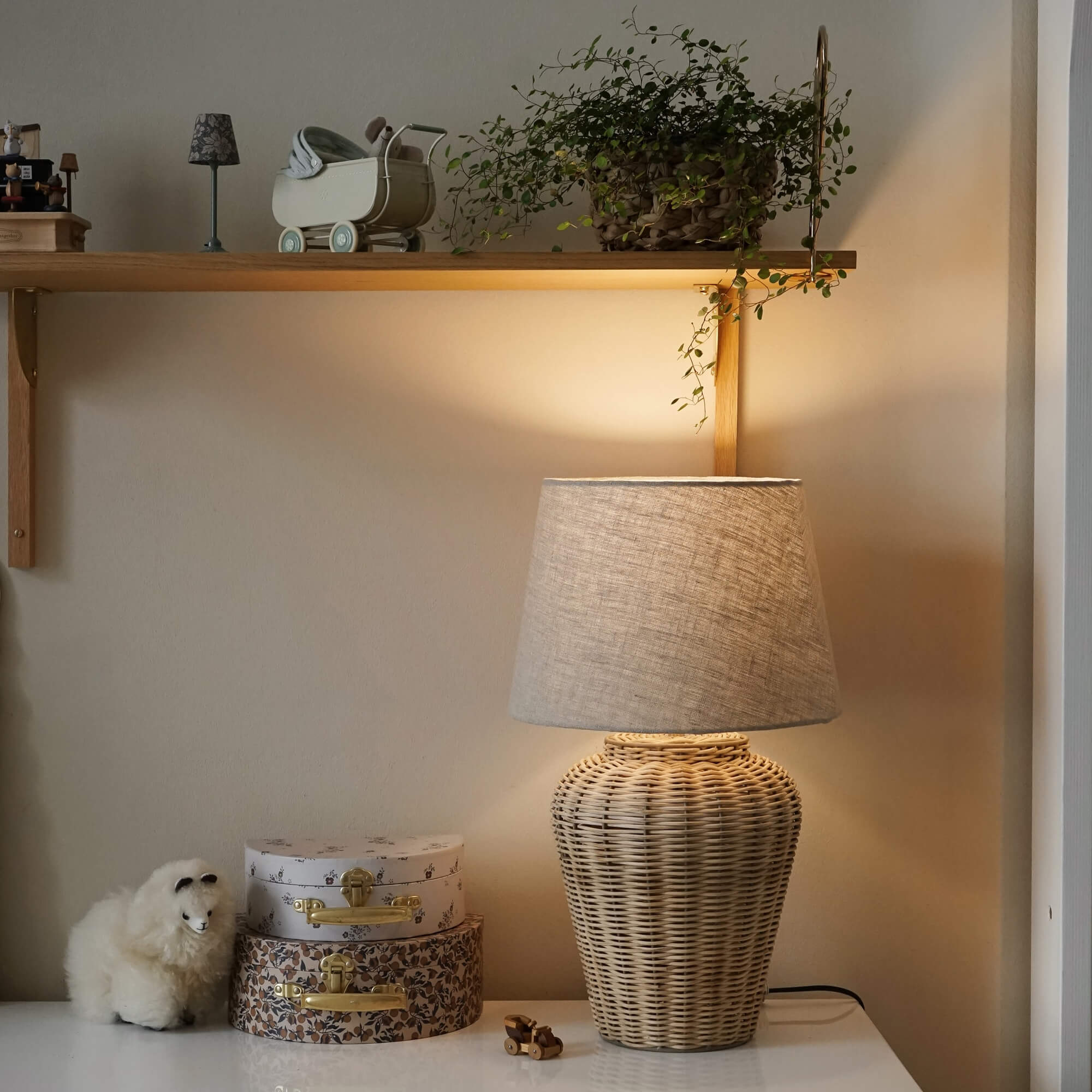 Tischlampe aus geflochtener Rattan mit beigem Stoffschirm auf weißem Tisch mit Dekoration und Pflanze