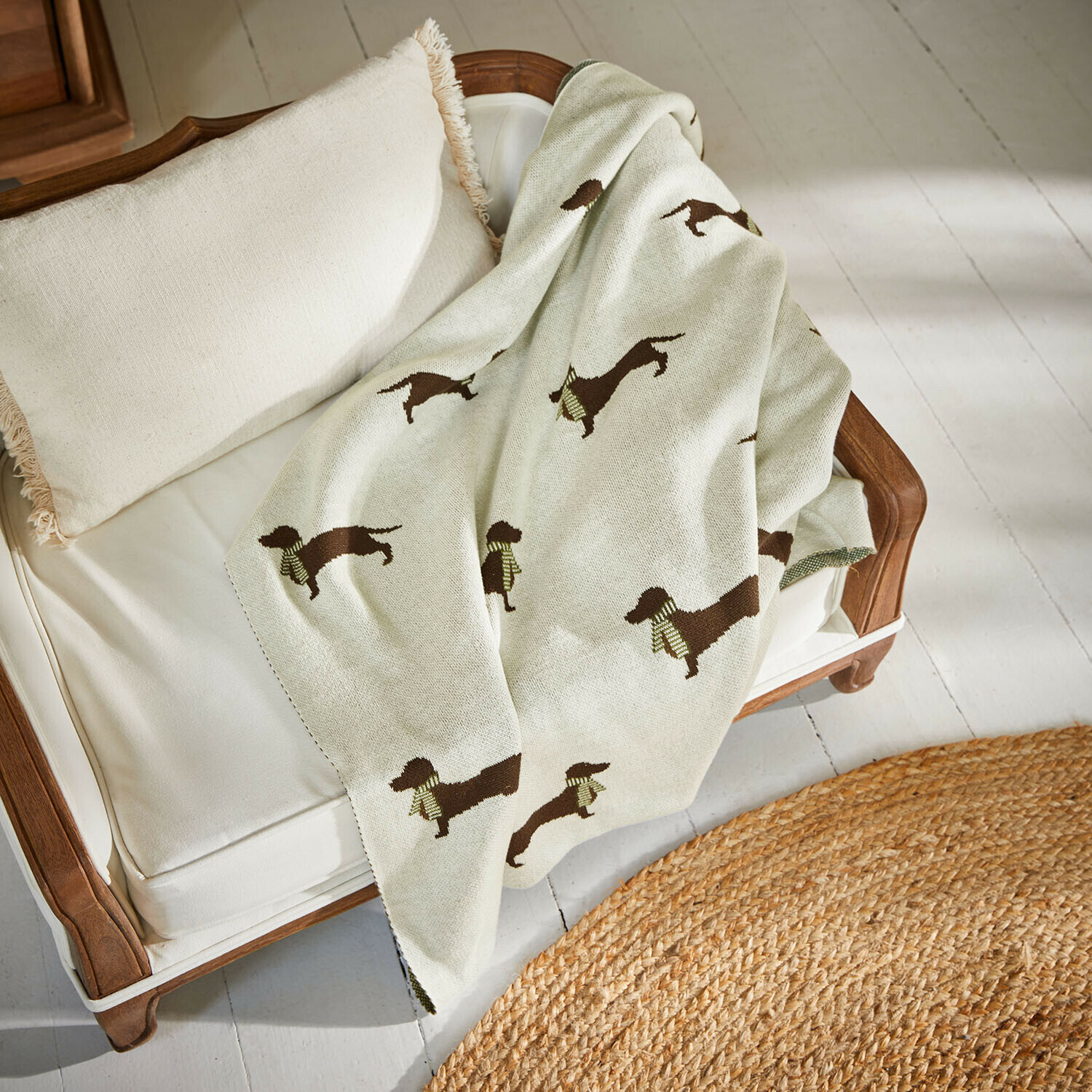 Hundedecke Brisette Beige Decke mit Dackel-Motiv auf weißem Sofa mit Holzrahmen und Fransen-Kissen