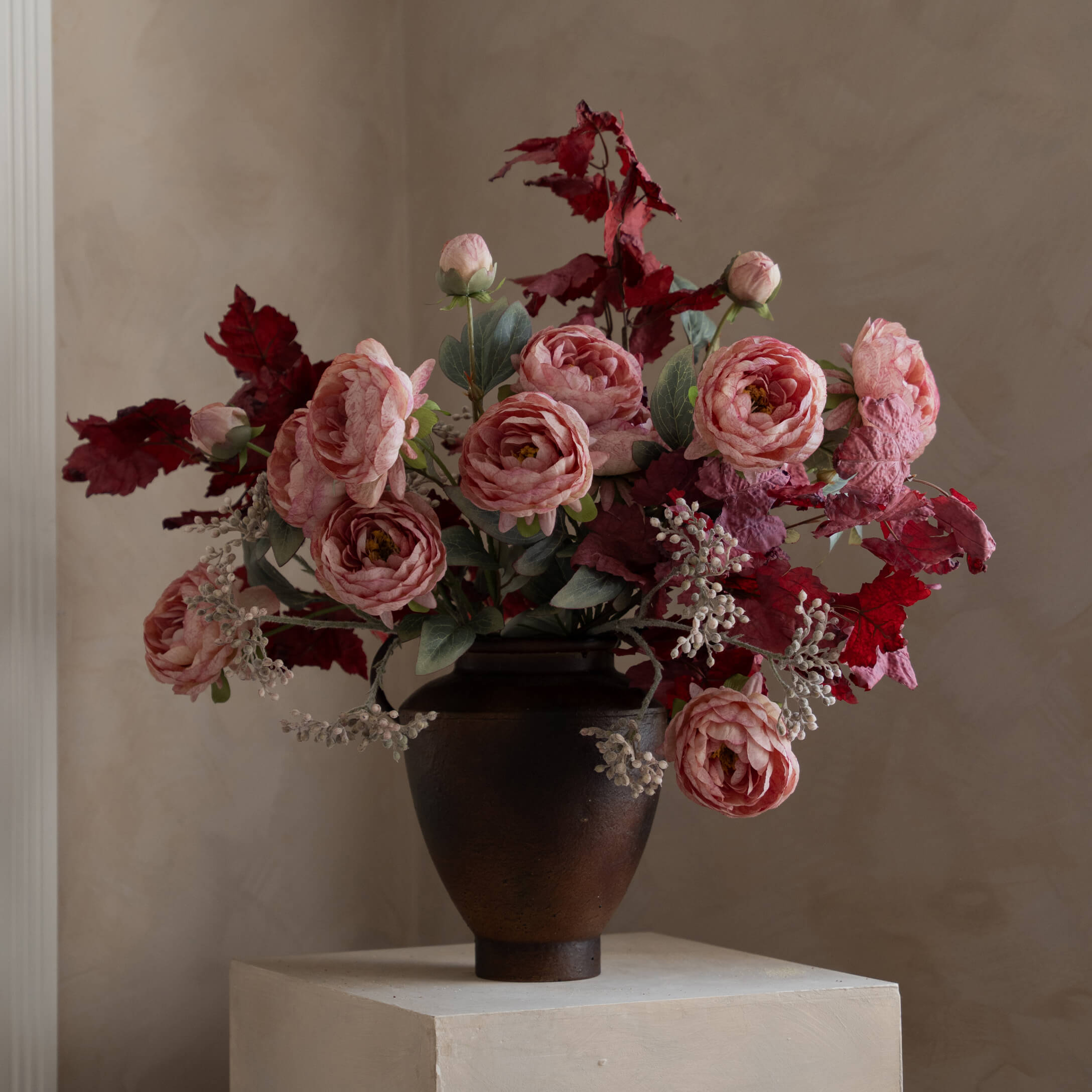 Strauß aus rosa Rosen und roten Blättern in dunklem Keramikvase auf hellem Podest
