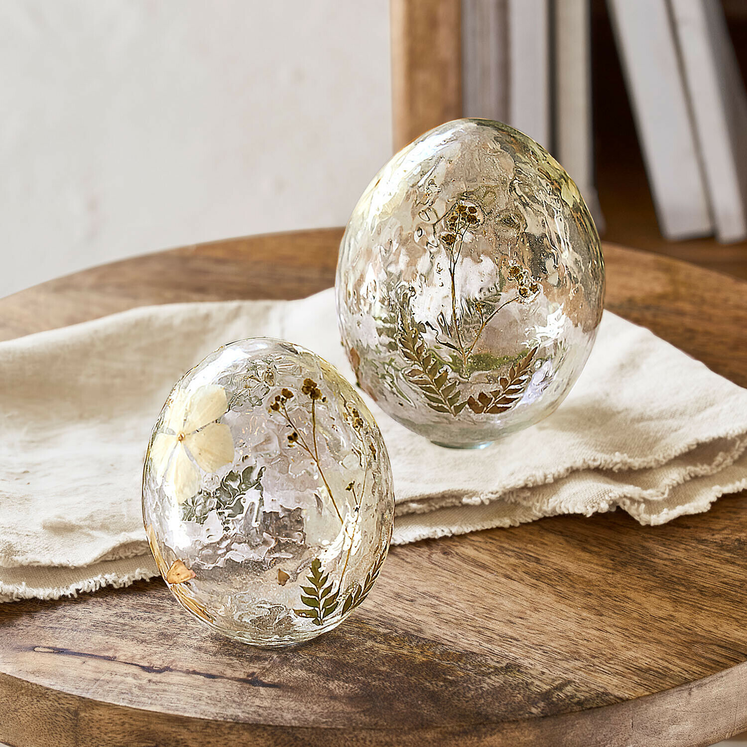 Glas-Eier mit getrockneten Blumen und Blättern als Dekoration auf Holztisch