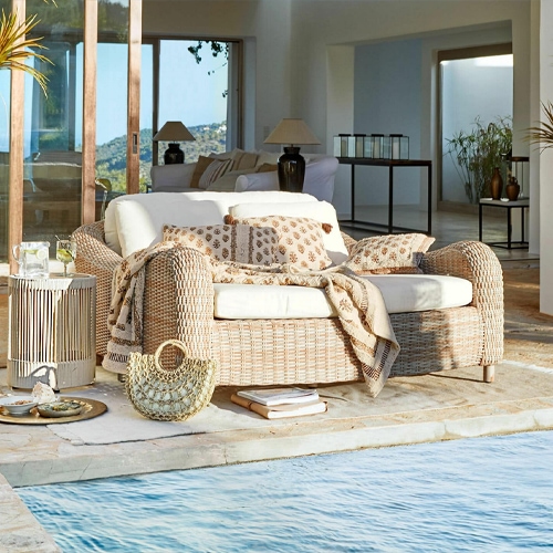Hell geflochtenes Rattan-Sofa mit cremefarbenen Kissen und Decke am Pool, Gartenmöbel
