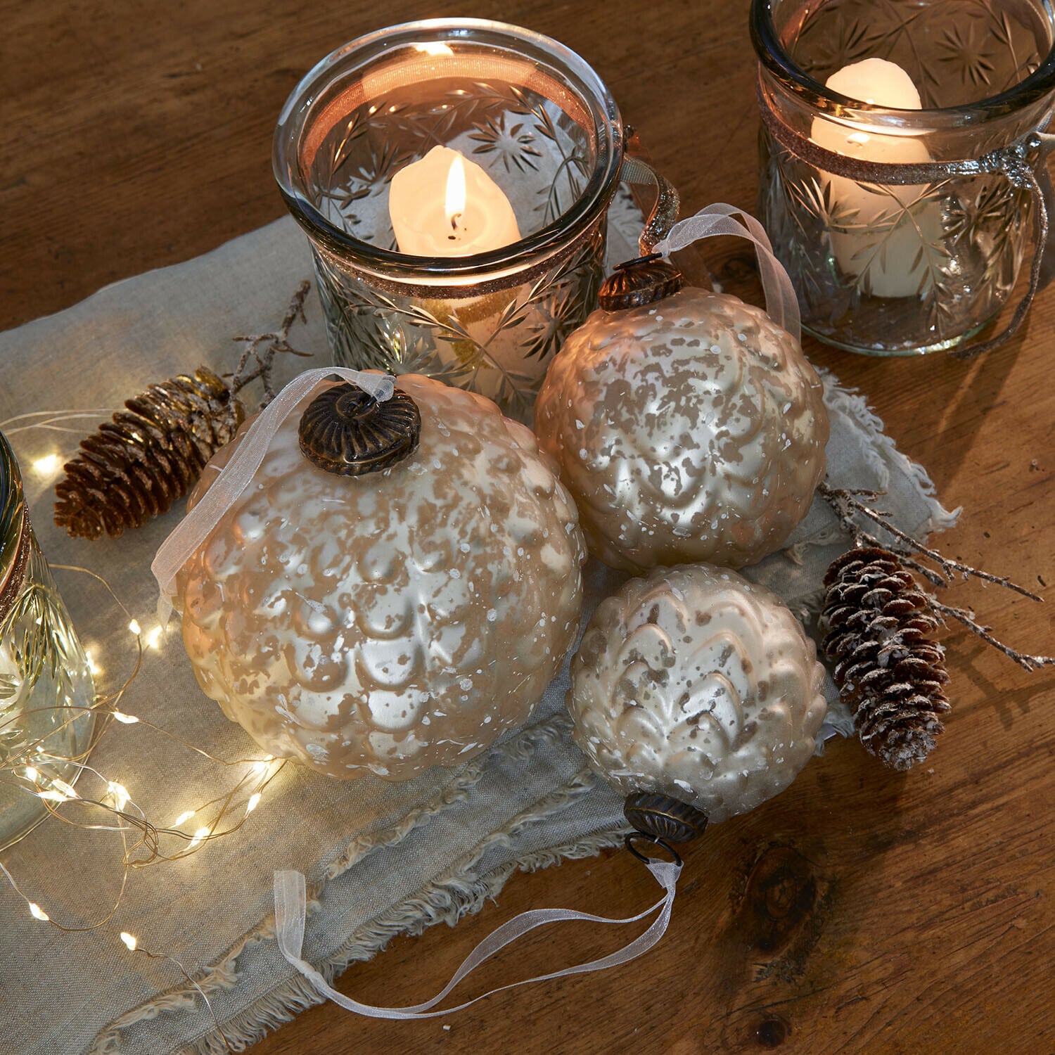 Weihnachtskugel 6er Set Domara Set aus drei perlmuttfarbenen Glas-Weihnachtskugeln mit dekorativem Muster und Kerzenlicht im Hintergrund