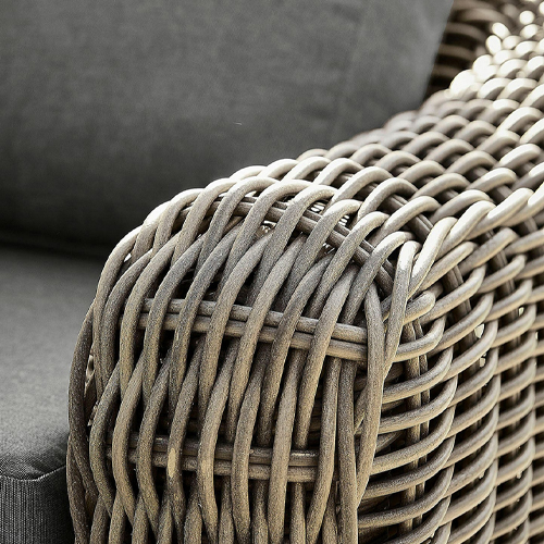 Nahaufnahme eines braunen, geflochtenen Polyrattan-Armlehne an einem Gartenmöbel mit grauem Kissen