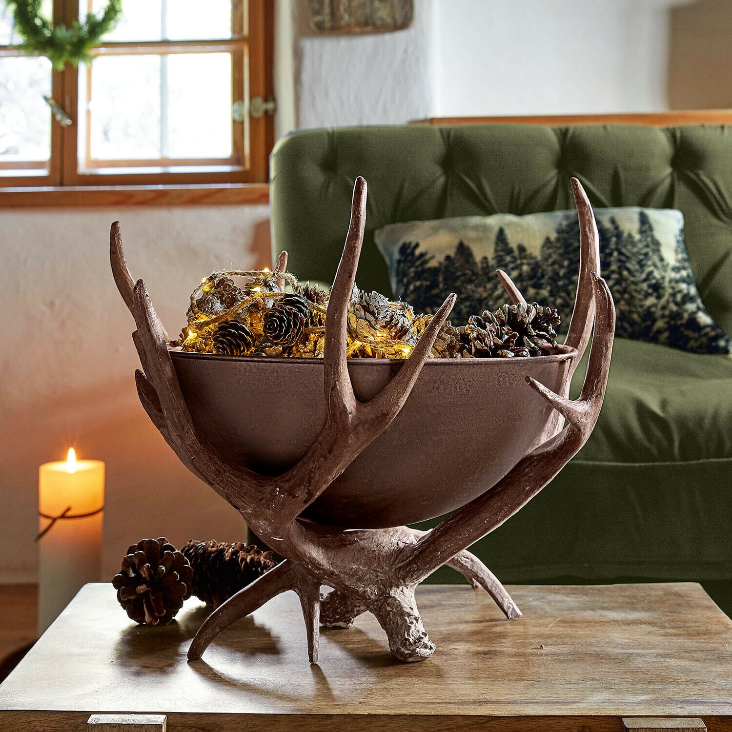 Dekorative Kupferschale mit Geweih, Tannenzapfen und Lichterkette auf Holztisch im Wohnzimmer