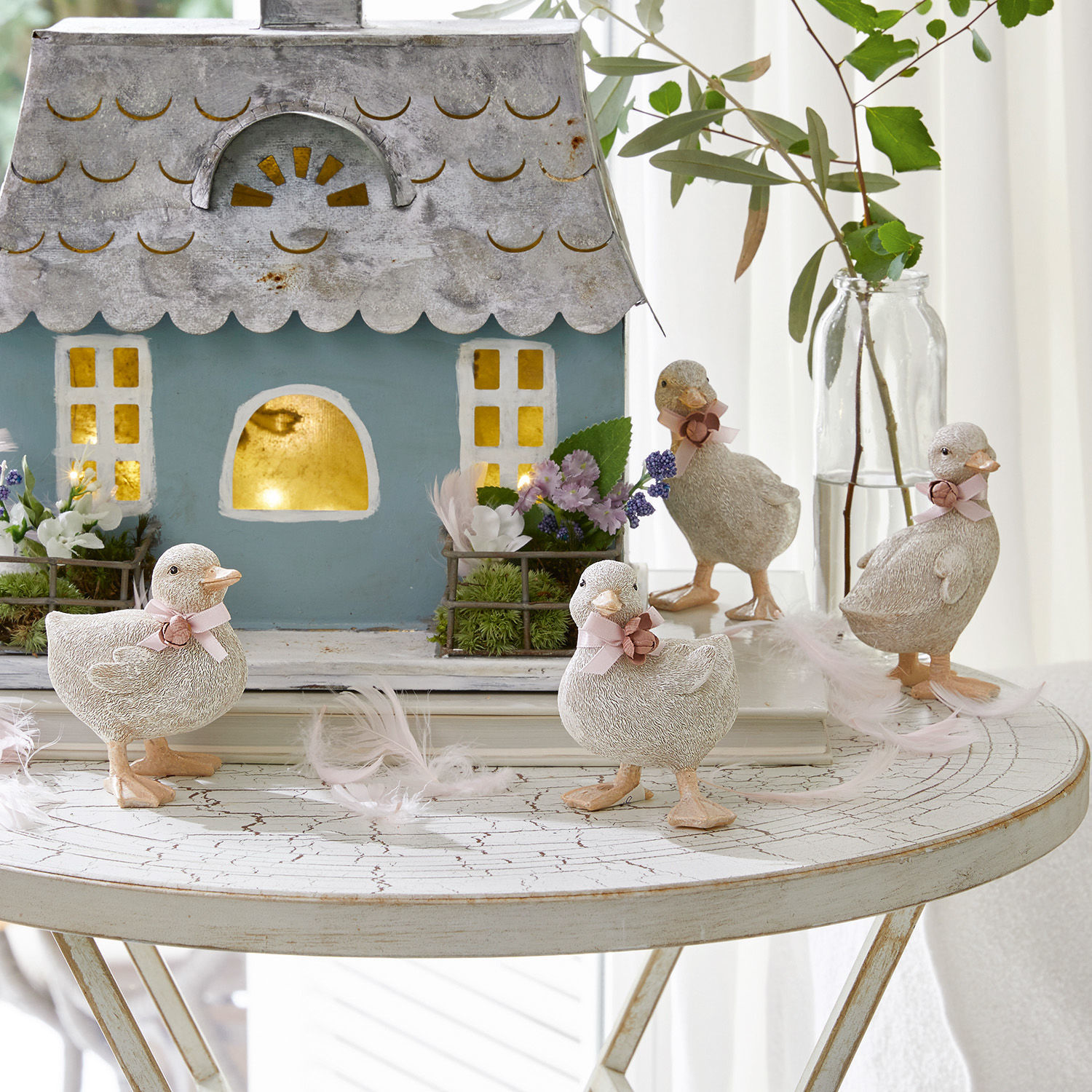 Küken 4er Set Orélie Dekorative Entenfiguren aus hellem Material auf weißem Tisch mit Haus und Blumenarrangement