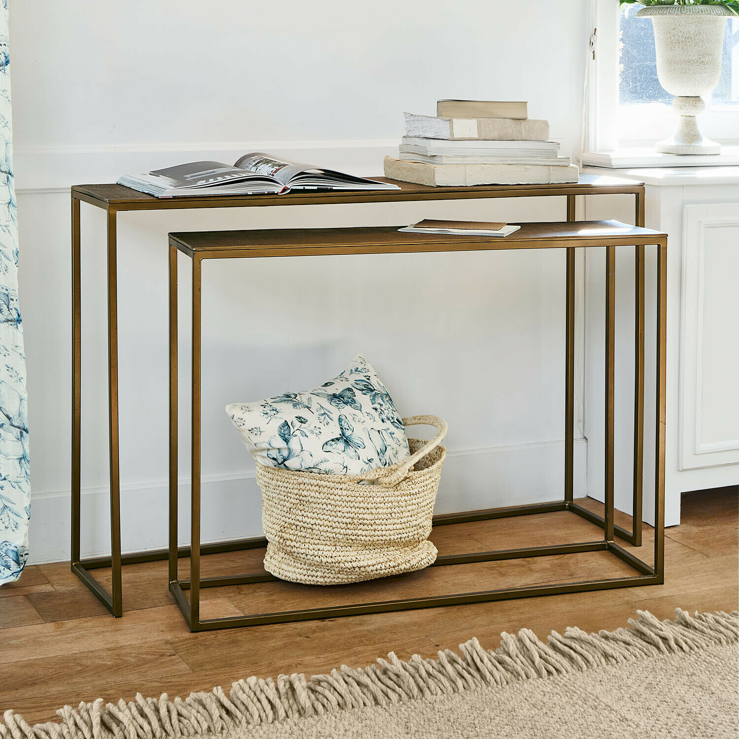 Zweiteiliges Set aus Metall-Beistelltischen in Messingoptik mit Büchern und Korb mit Kissen