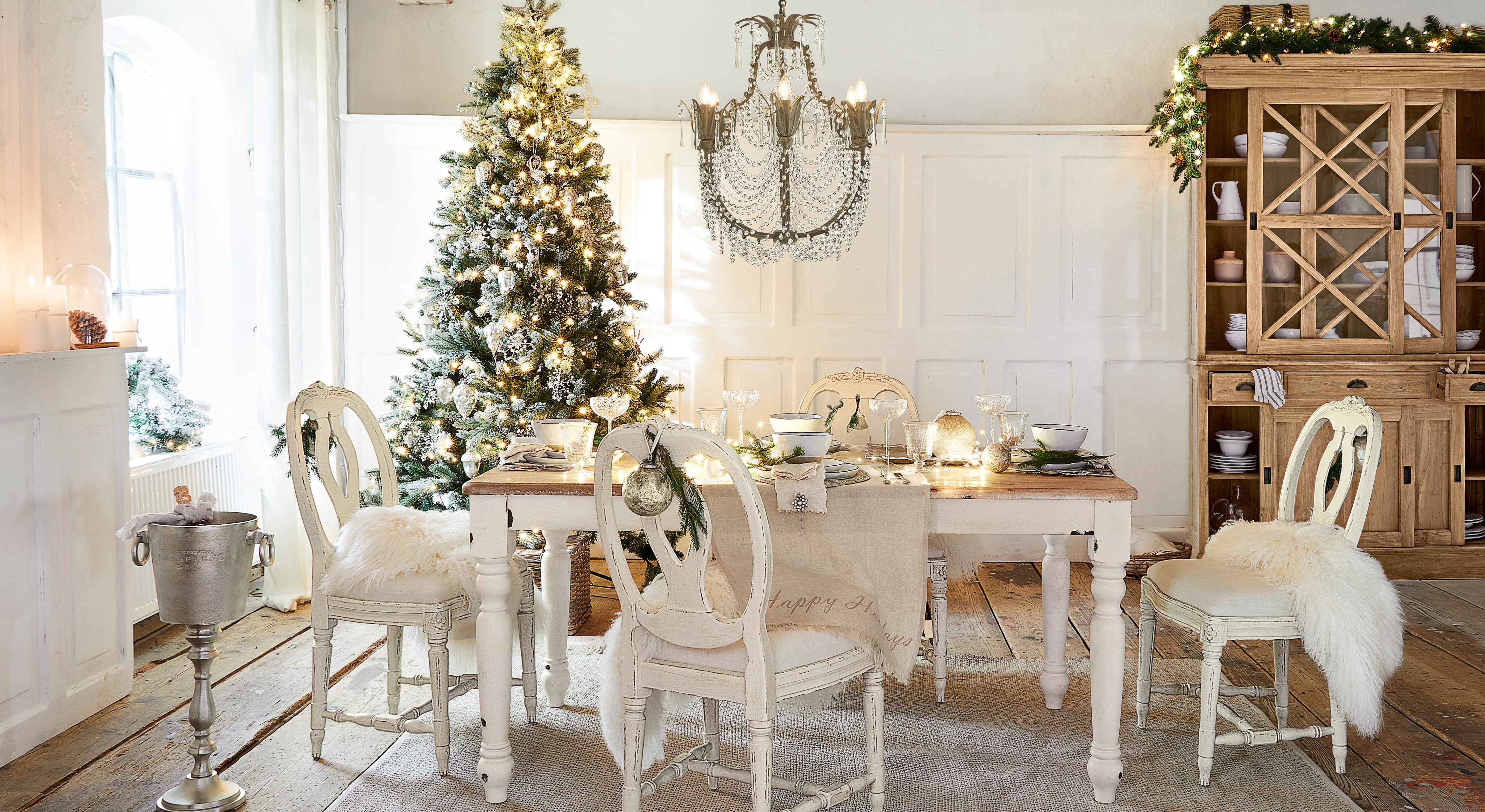 Esszimmer mit weißem Holztisch und Stühlen, festlich dekoriert mit Weihnachtsbaum und Kristallleuchter