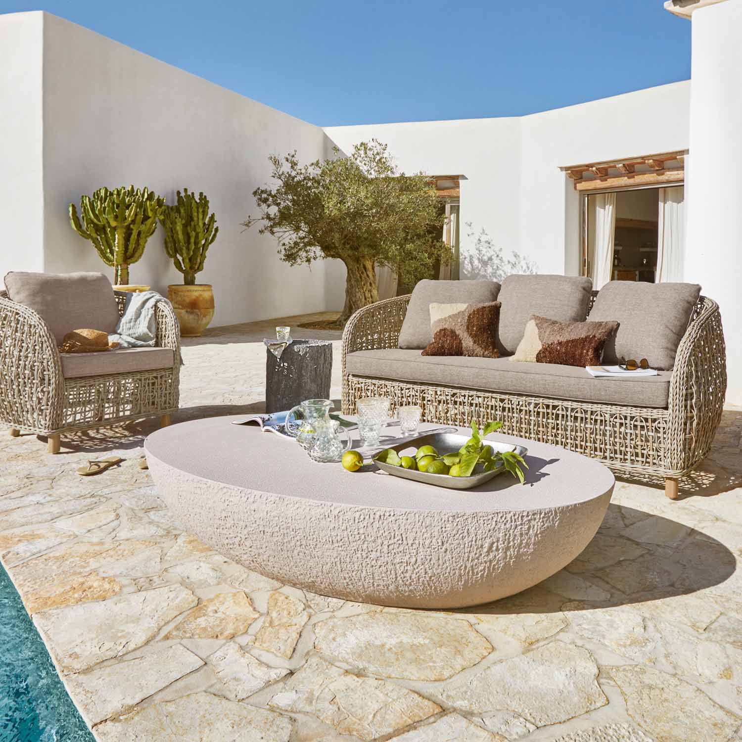 Gartenmöbel-Set aus beigem Rattan mit Polstern und steinernem Tisch auf Terrasse am Pool