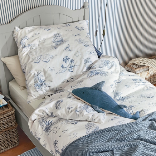 Bettwäsche aus Baumwolle in Weiß mit blauen Meeresmotiven auf grauem Bett mit Haifischkissen