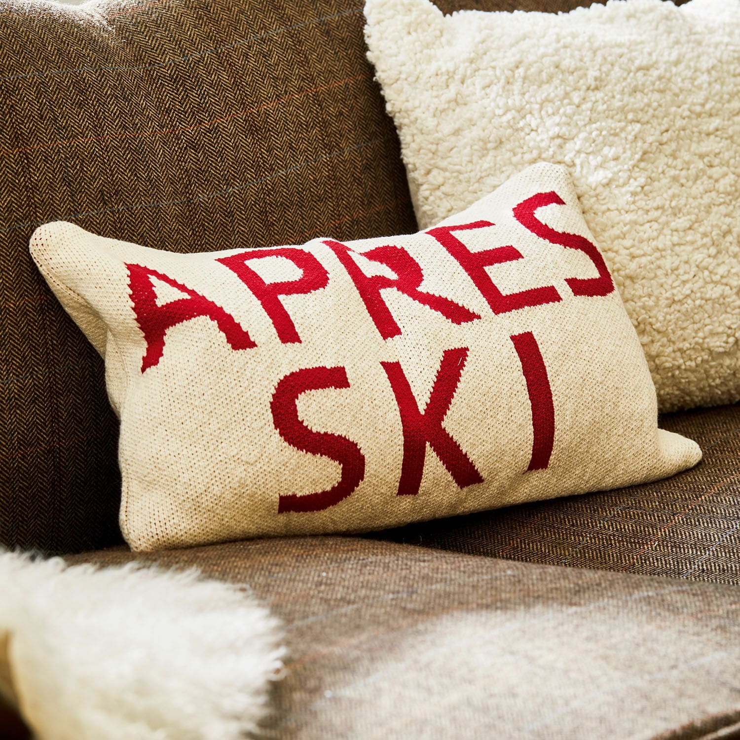 Kissenhülle Apres Ski Beiges Kissen mit rotem Schriftzug Apres Ski auf braunem Sofa mit weichem Fellplaid