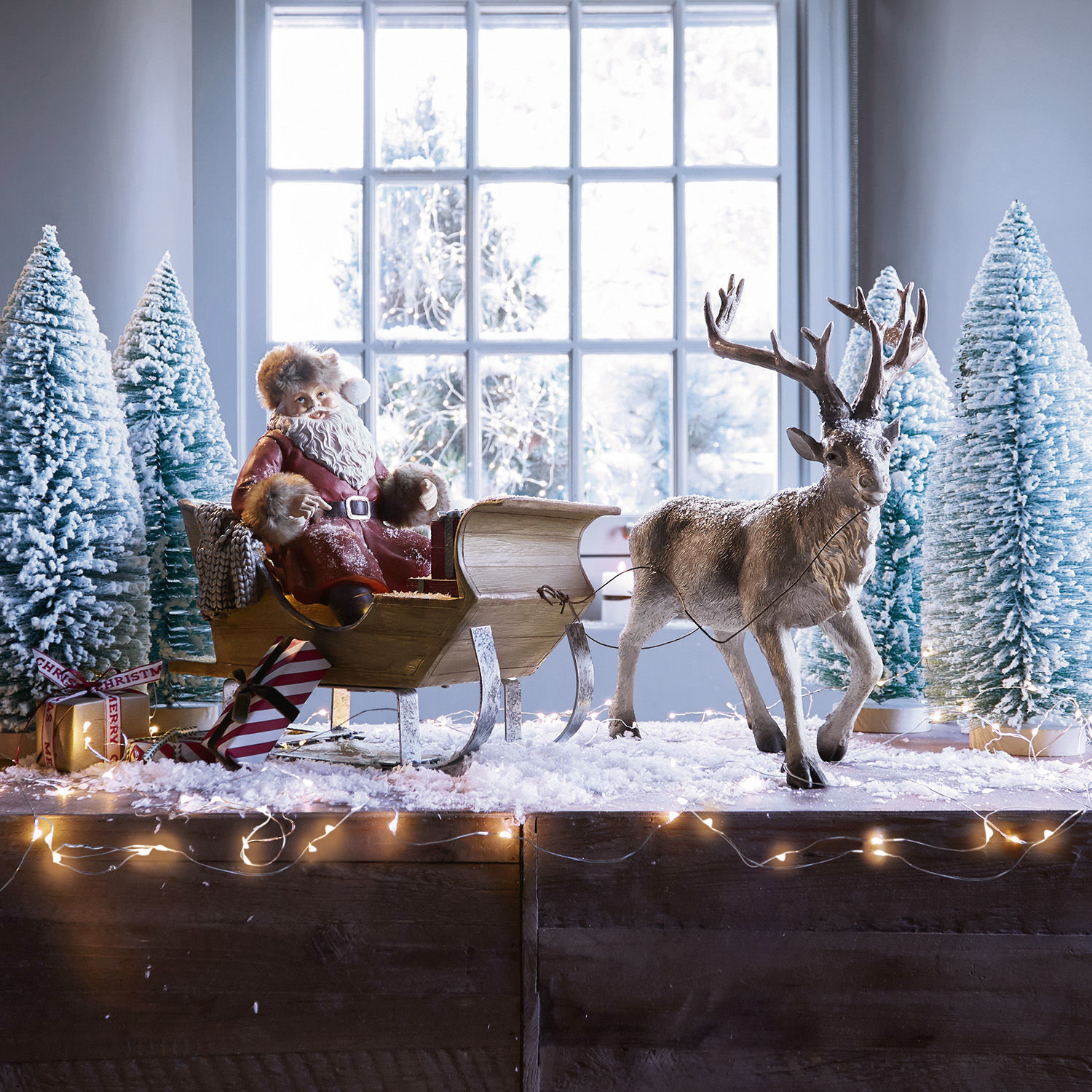 Weihnachtsschlitten Palaima Weihnachtsfigur Santa Claus im roten Mantel auf Holzschlitten mit Rentier und schneebedeckten Tannen