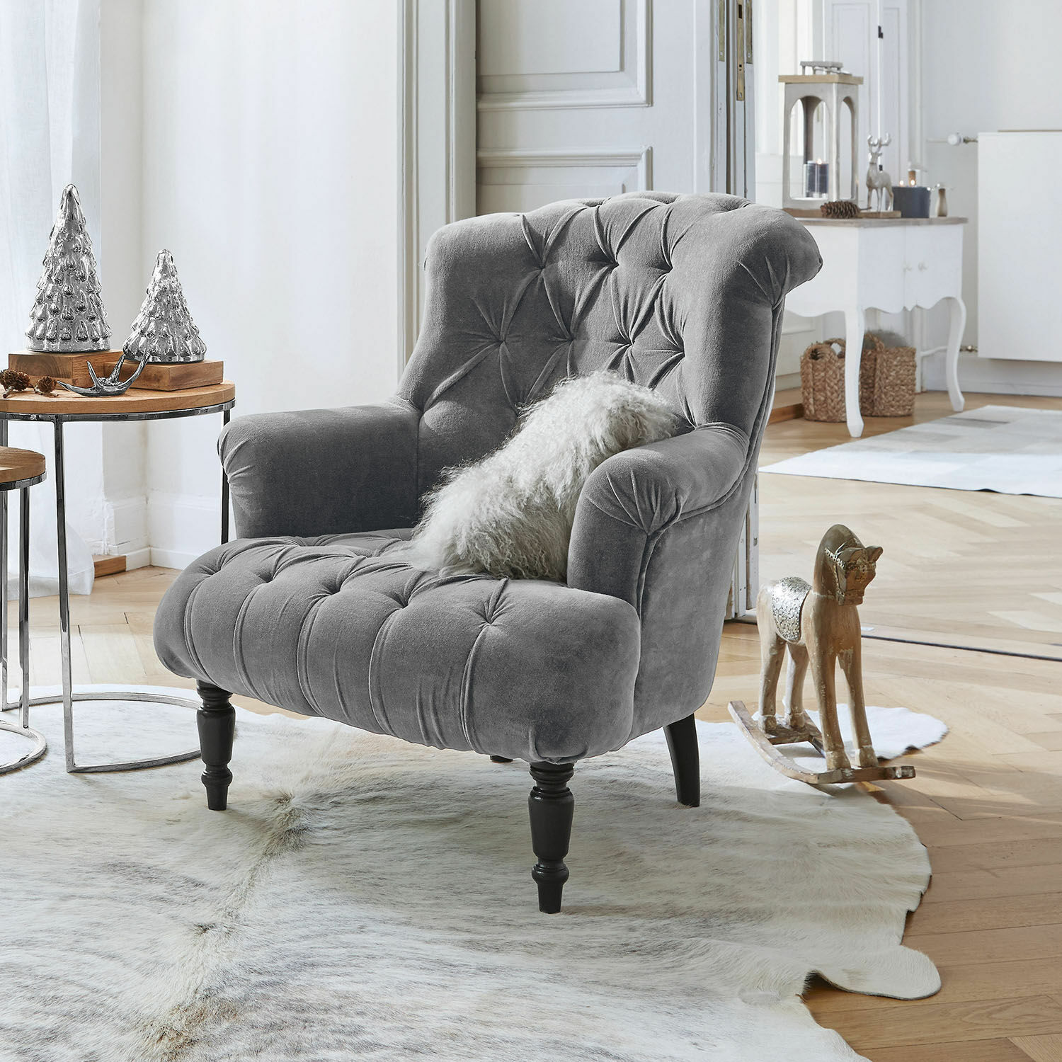 Grau gepolsterter Samtfotel mit Knopfheftung und schwarzen Holzbeinen in hellem Wohnzimmer mit Dekoration
