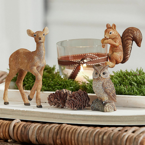 Dekorative Tierfiguren aus Holz mit Glaswindlicht und Kerze auf grünem Moos, natürliche Tischdeko