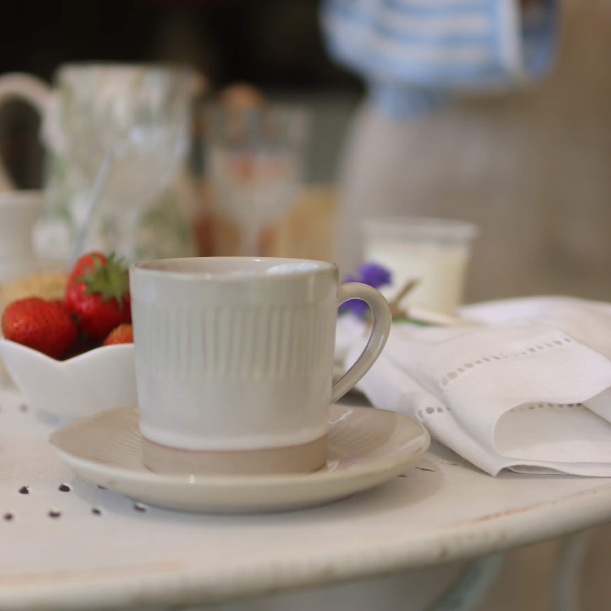 Beige Keramiktasse mit Untertasse auf weißem Tisch mit Erdbeeren und Leinenserviette