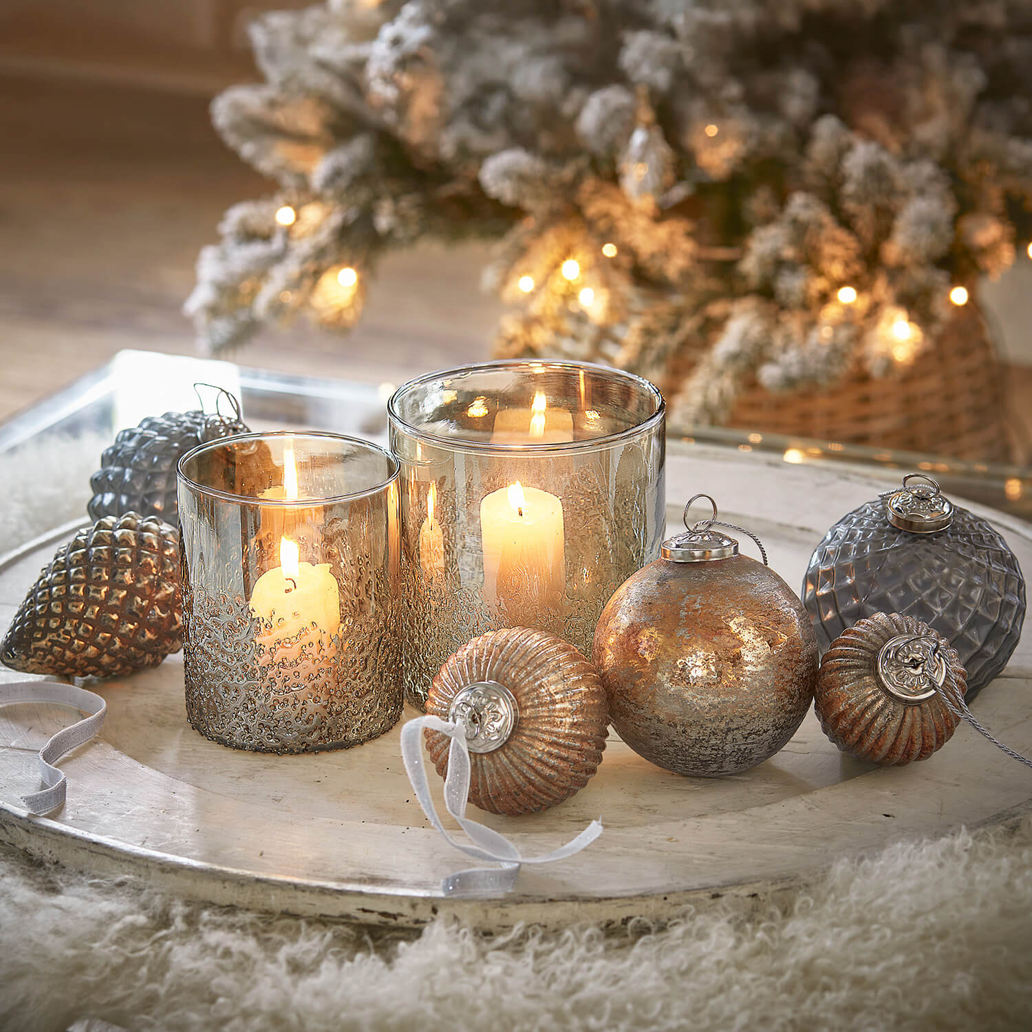 Gläserne Windlichter und metallische Weihnachtskugeln in Gold- und Silbertönen auf dekorativem Tablett