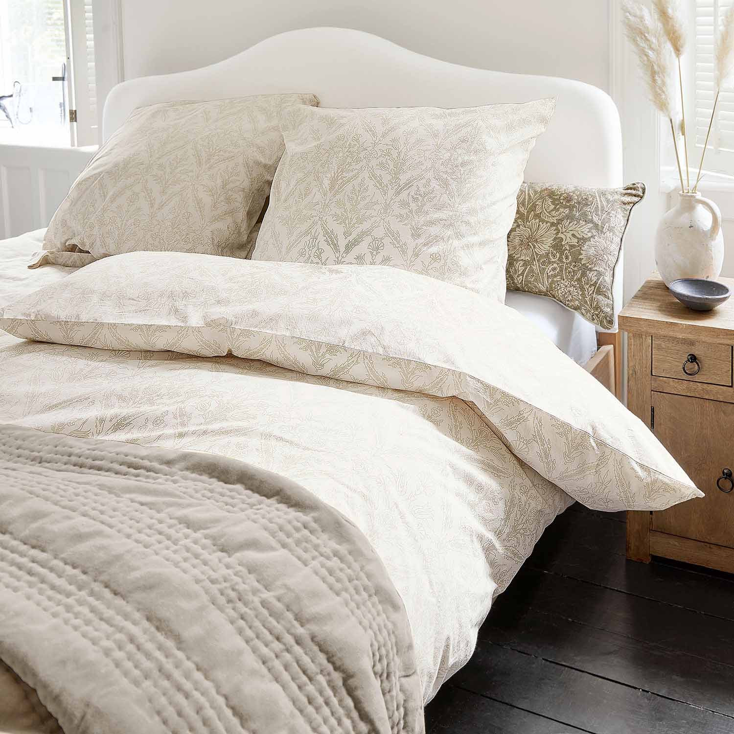 Helle Baumwollbettwäsche mit zartem Pflanzenmuster und weiche Decke in gemütlichem Schlafzimmer