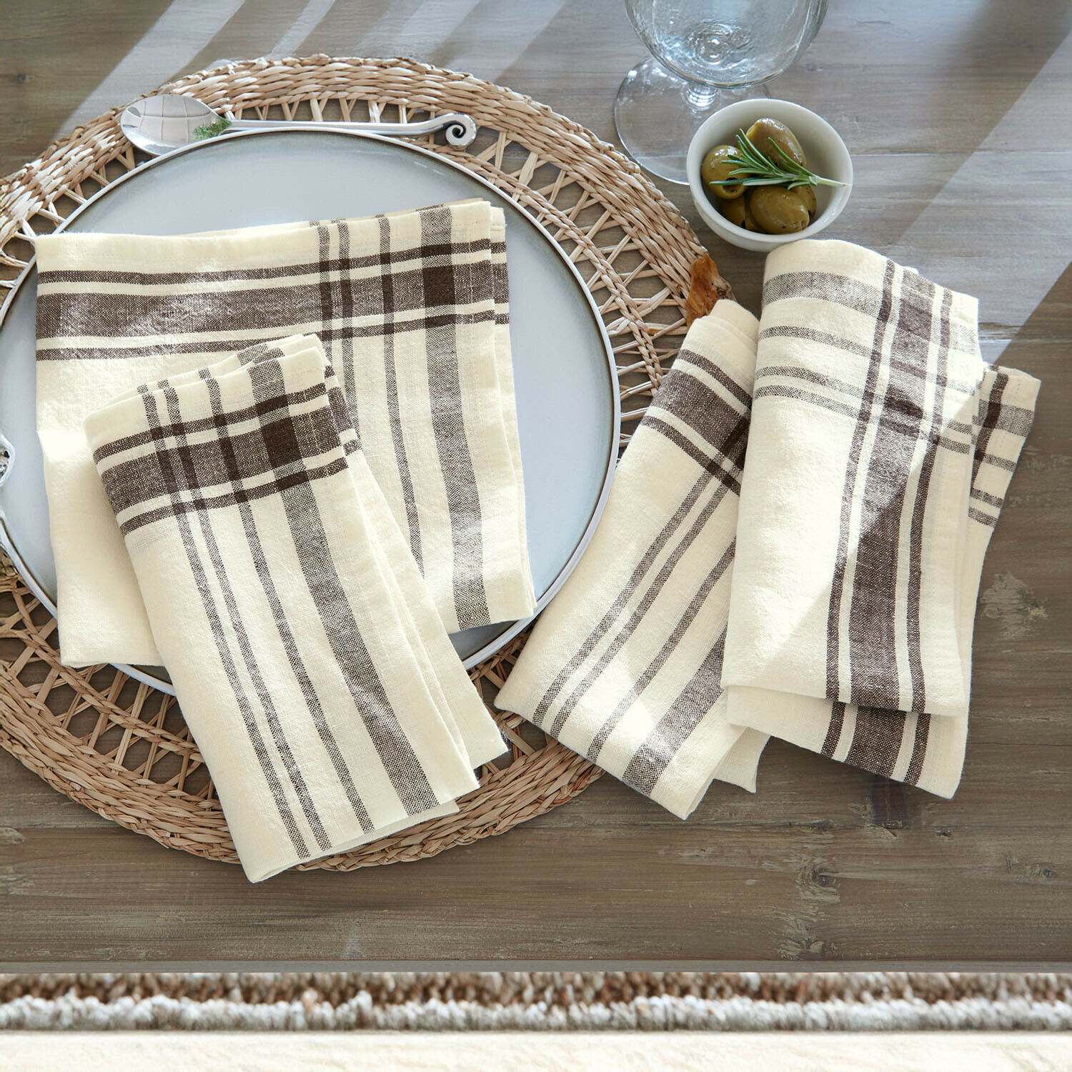 Leinenservietten in Creme mit braunem Karomuster auf rustikalem Holztisch arrangiert
