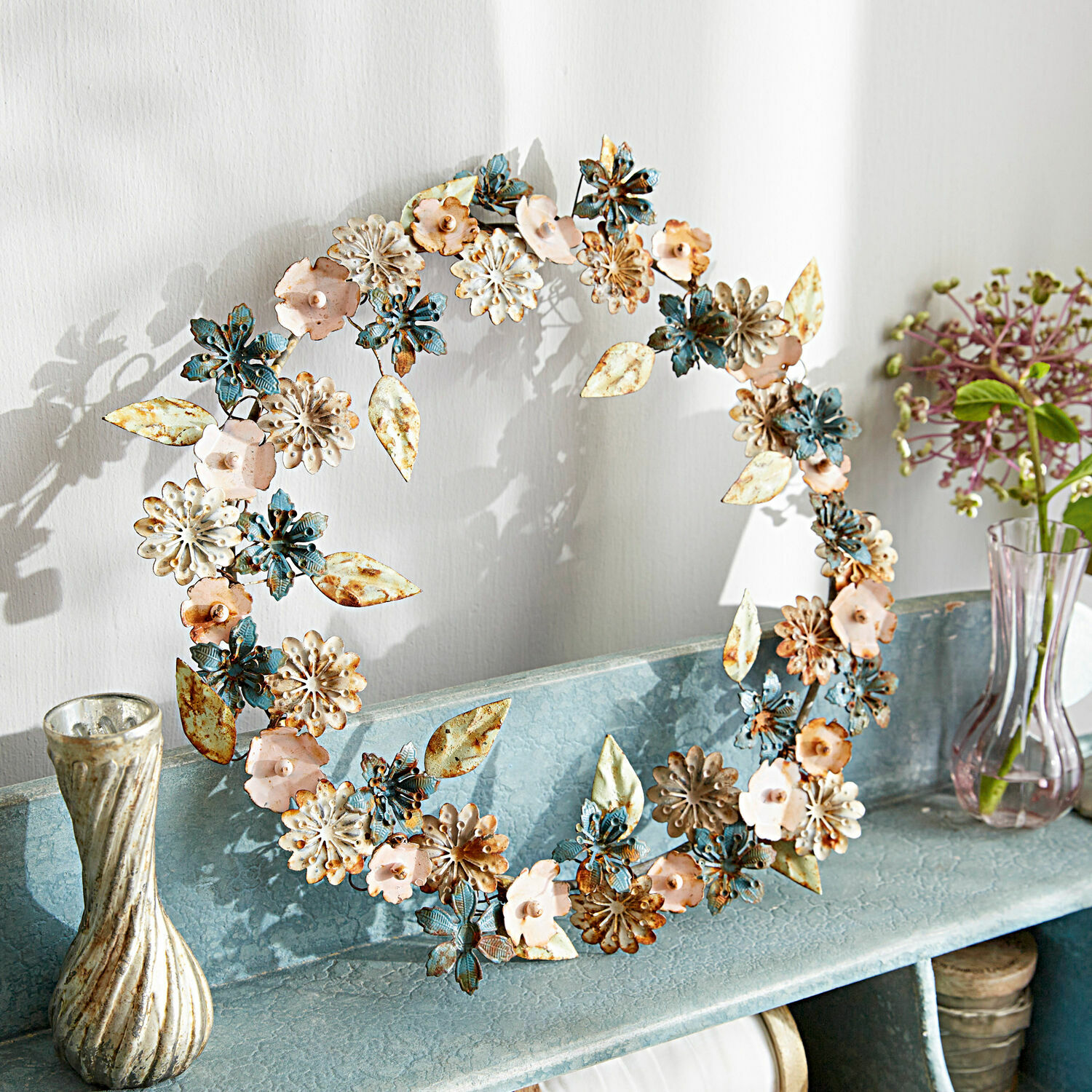Dekorativer Metallkranz in Blau, Rosa und Cremefarben auf Regal für Wohnraumdeko