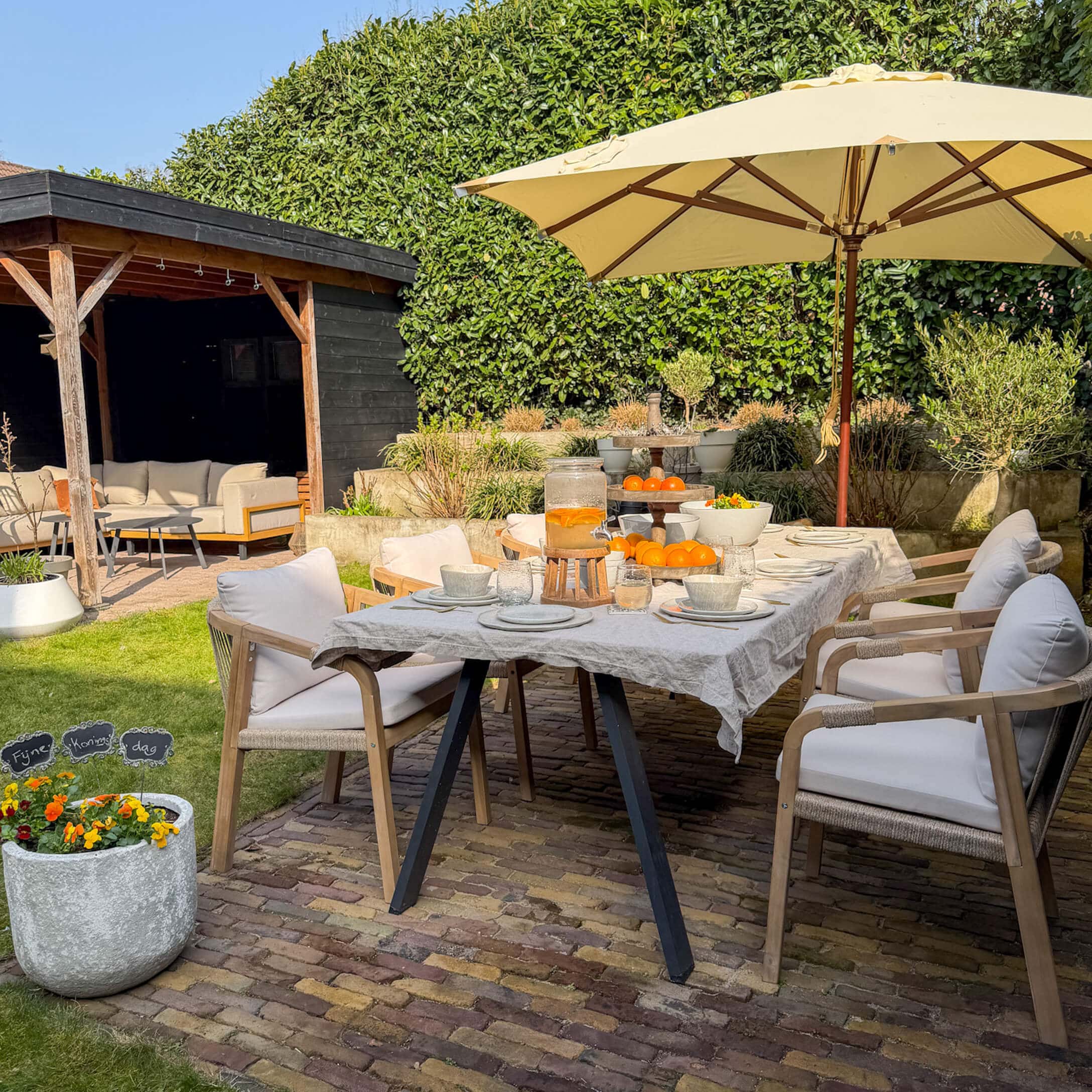 Gartenmöbel-Set mit Holzstühlen und beigem Sonnenschirm auf gepflasterter Terrasse mit Orangen