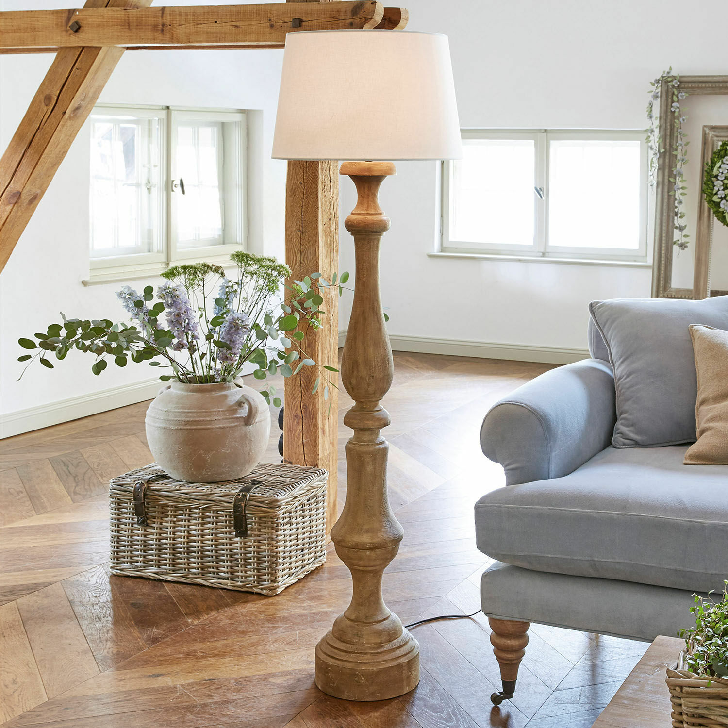 Stehlampe Etienne Holz-Stehlampe mit weißem Lampenschirm in hellem Wohnzimmer mit blauem Sofa und Korb aus Weide