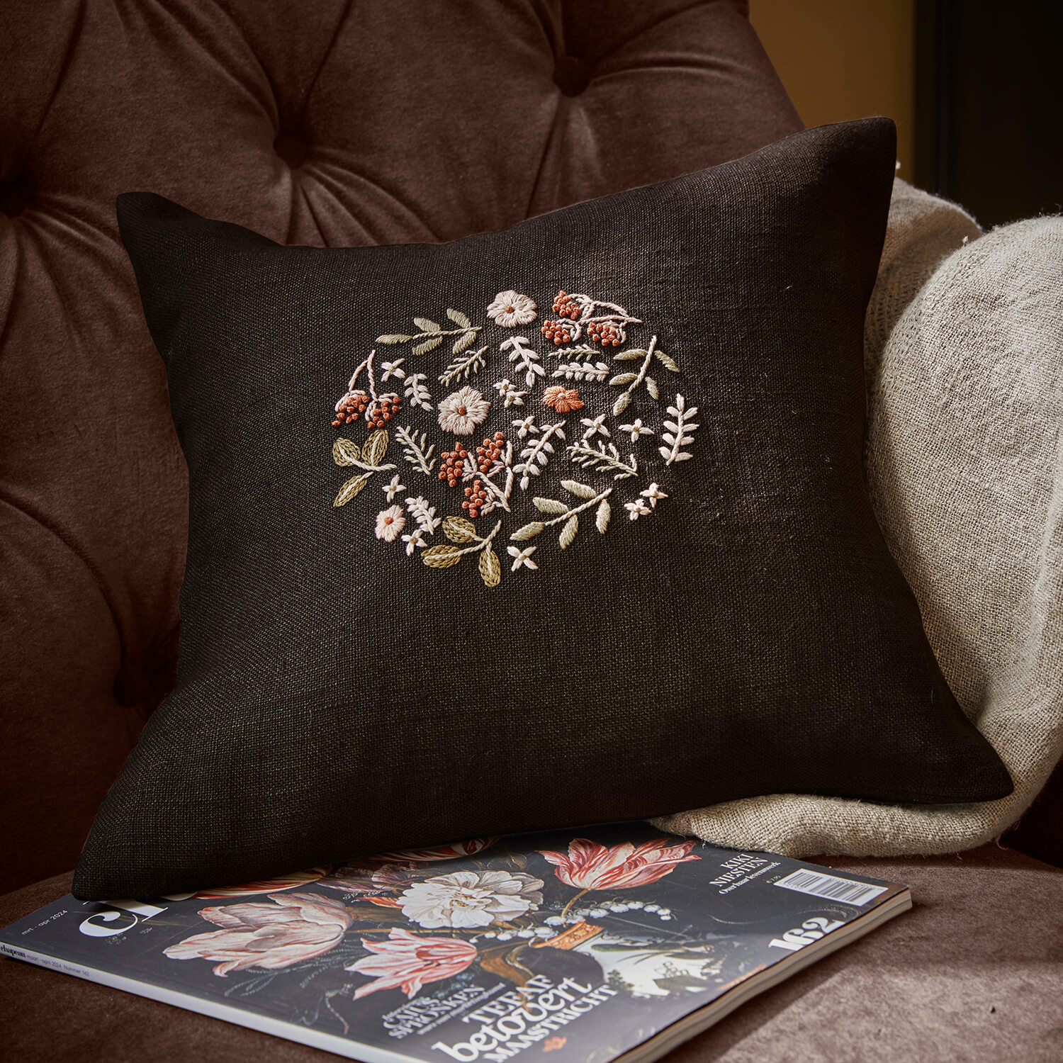 Schwarzes Leinenkissen mit pastellfarbenem Blumenstickmuster auf Sessel mit Magazin