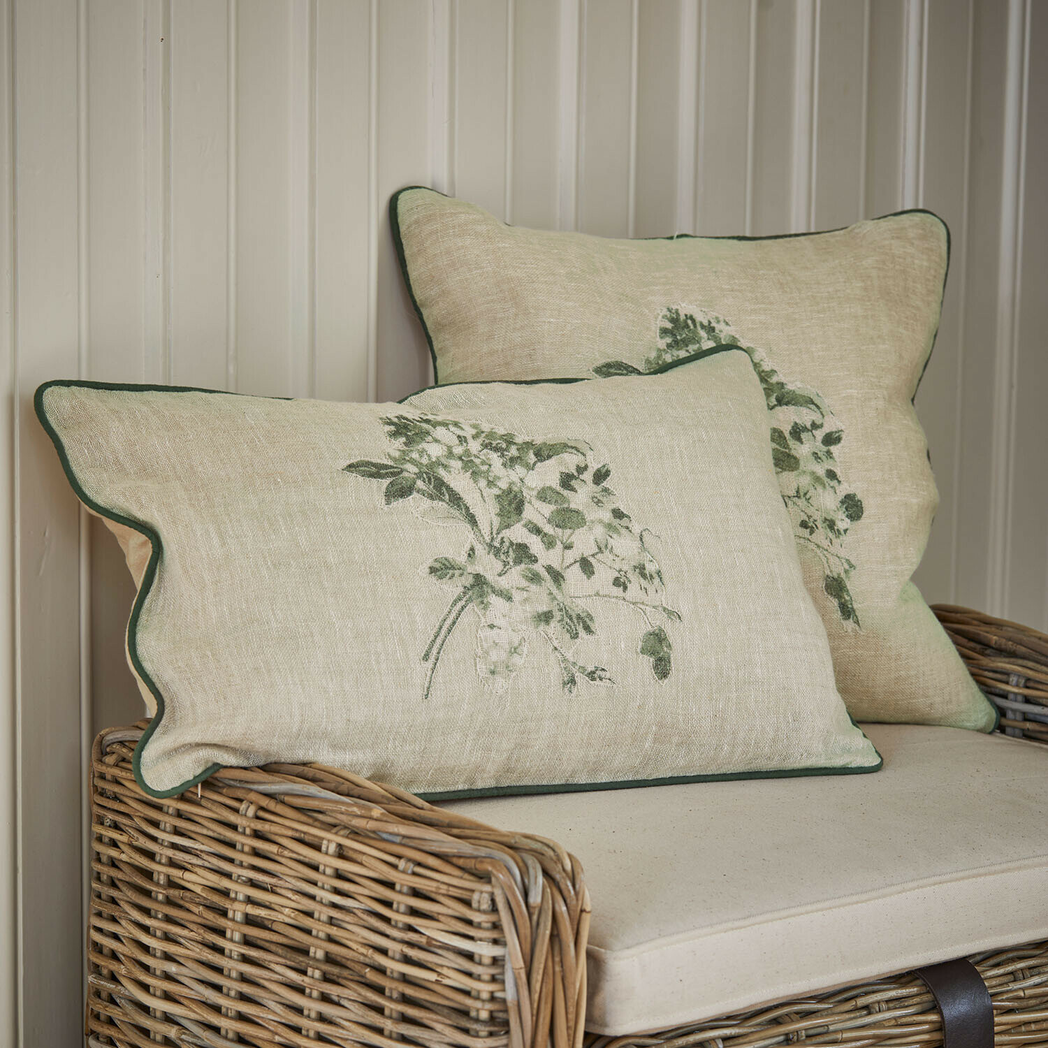 Beige Leinenkissen mit grünem Pflanzenmuster und grünem Rand auf Rattansofa