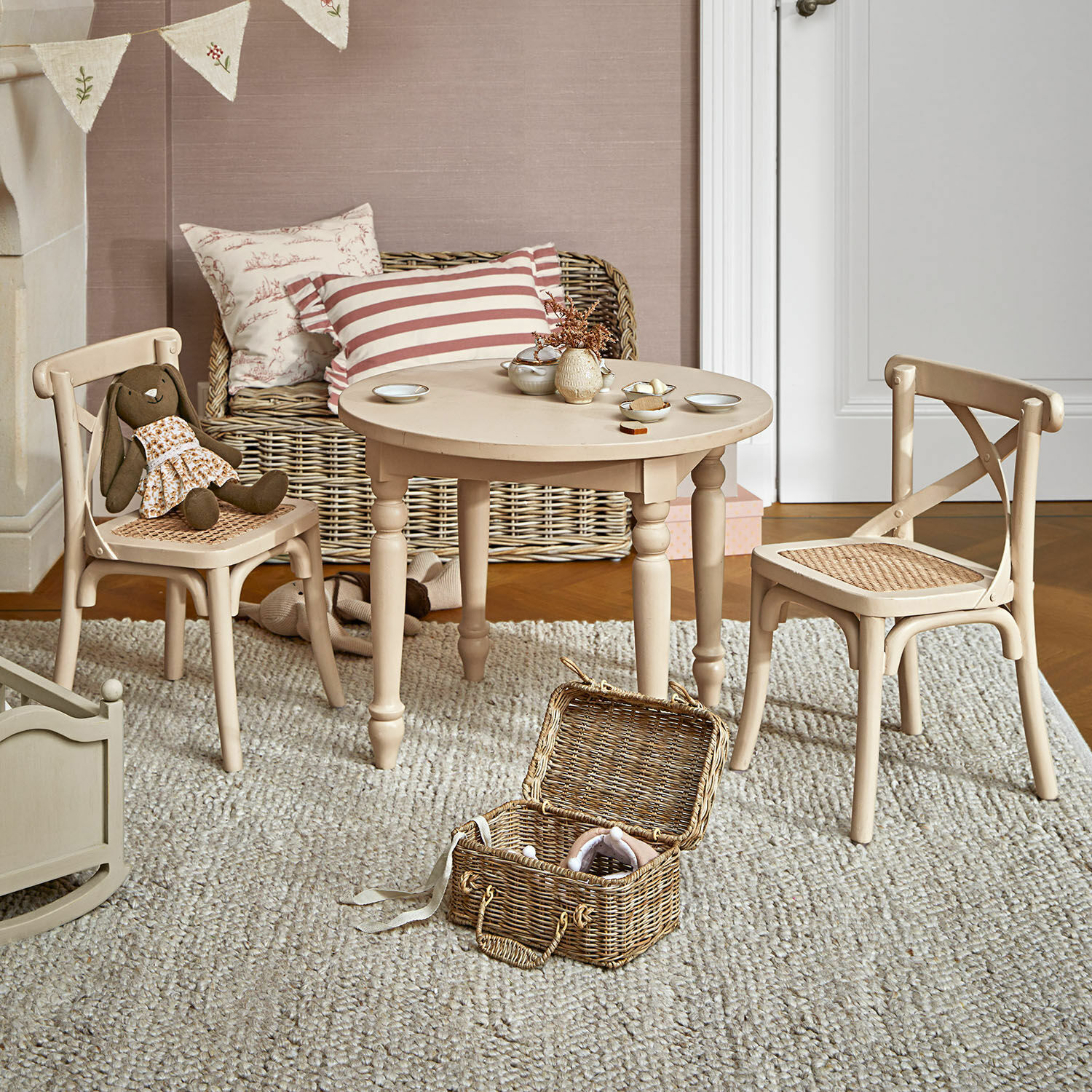 Kindersitzgruppe Sourila Beiger Holztisch mit zwei Stühlen und geflochtenen Sitzen in einem Kinderzimmer mit Spielzeug und Teppich