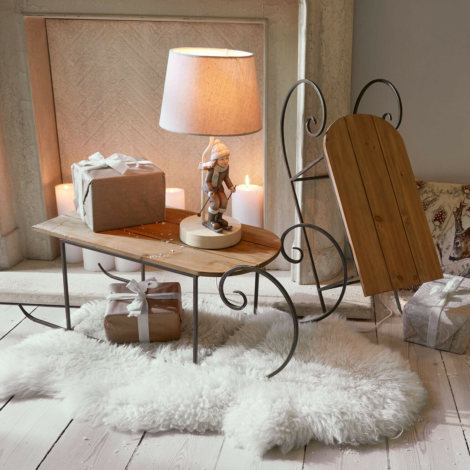 Schlittenförmiger Beistelltisch aus Holz und Metall mit Lampe und Geschenken auf weißem Fellteppich