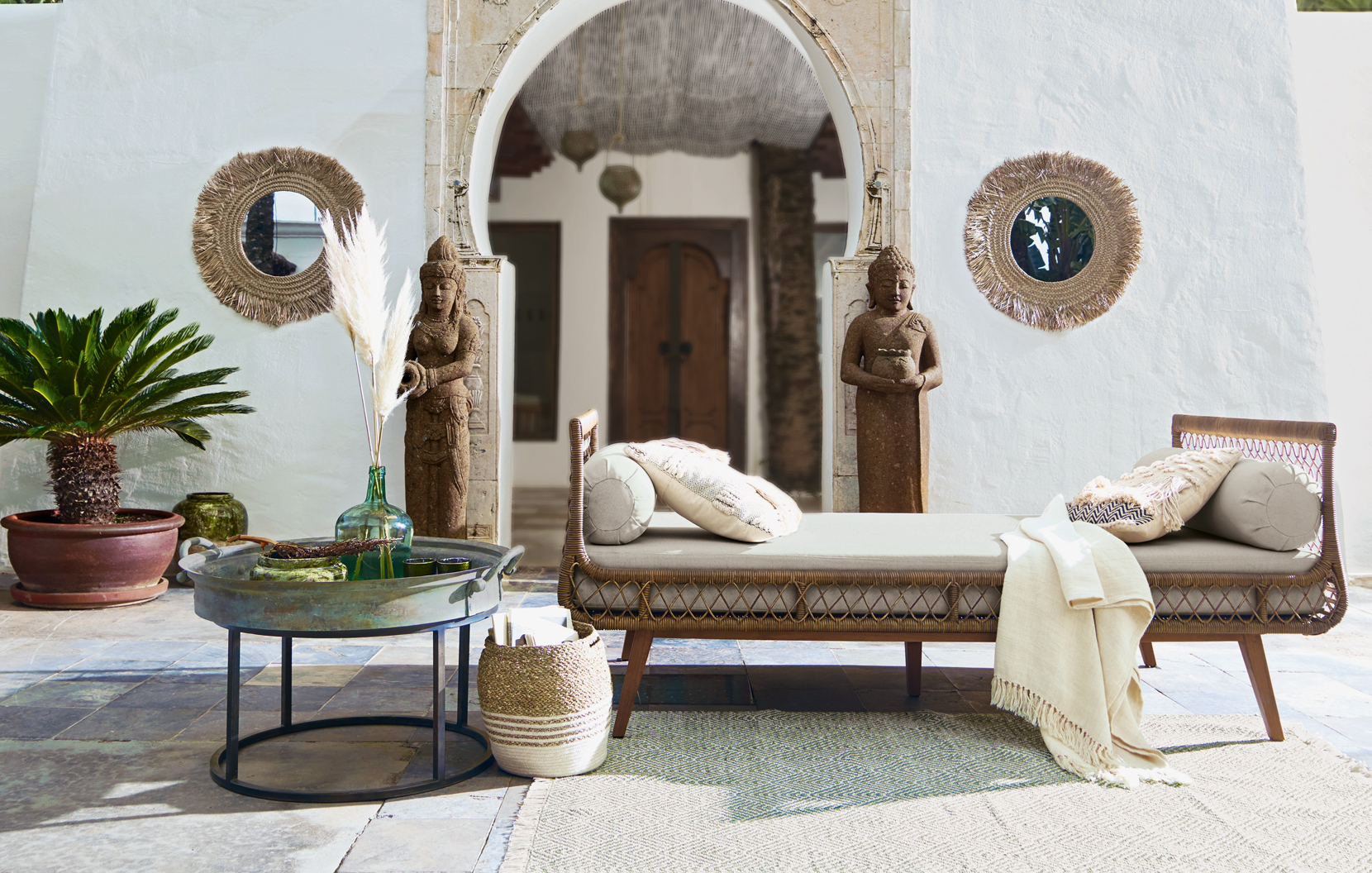Orientalisches Wohnzimmer mit beiger Rattan-Liege, Steinskulpturen und Spiegeln aus Seegras