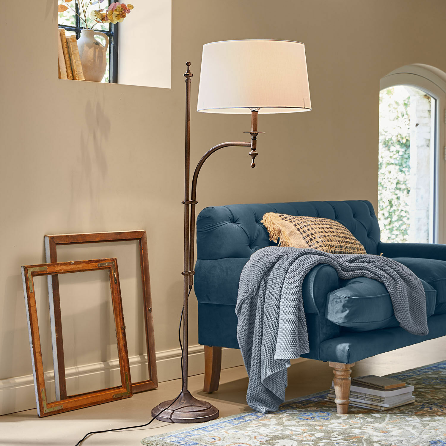 Stehlampe Salvaterre Stehlampe aus Metall mit weißem Lampenschirm neben blauem Sofa und zwei Holzrahmen an der Wand.