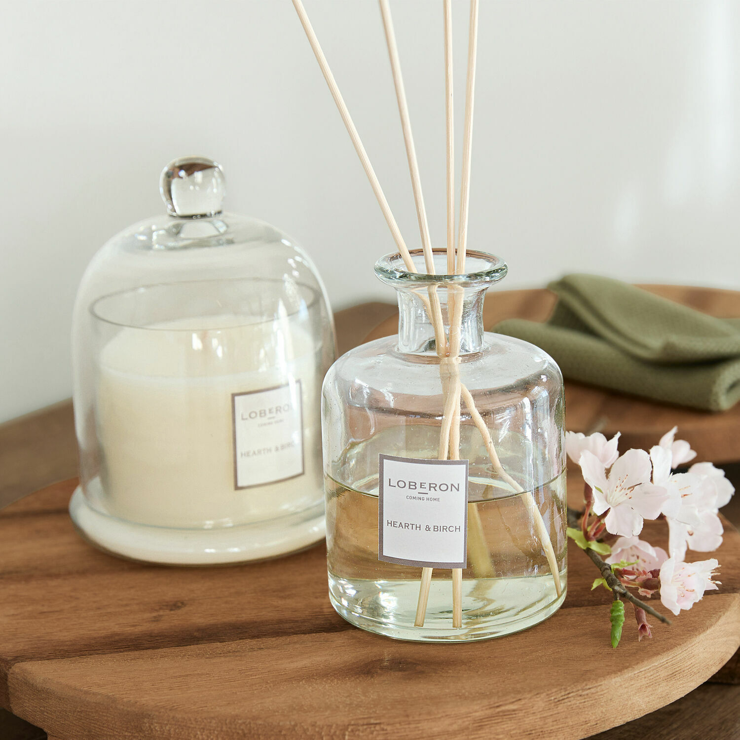 Duftset Vanis Glas-Duftspender Hearth & Birch mit Stäbchen auf Holztisch, weiße Kerze unter Glasglocke