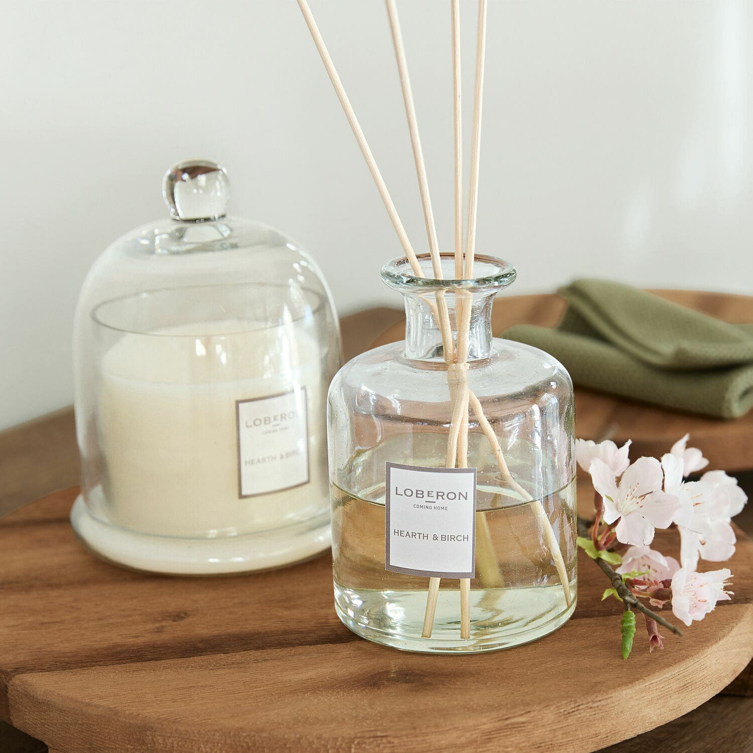 Duftset Vanis Glas-Duftspender Hearth & Birch mit Stäbchen auf Holztisch, weiße Kerze unter Glasglocke