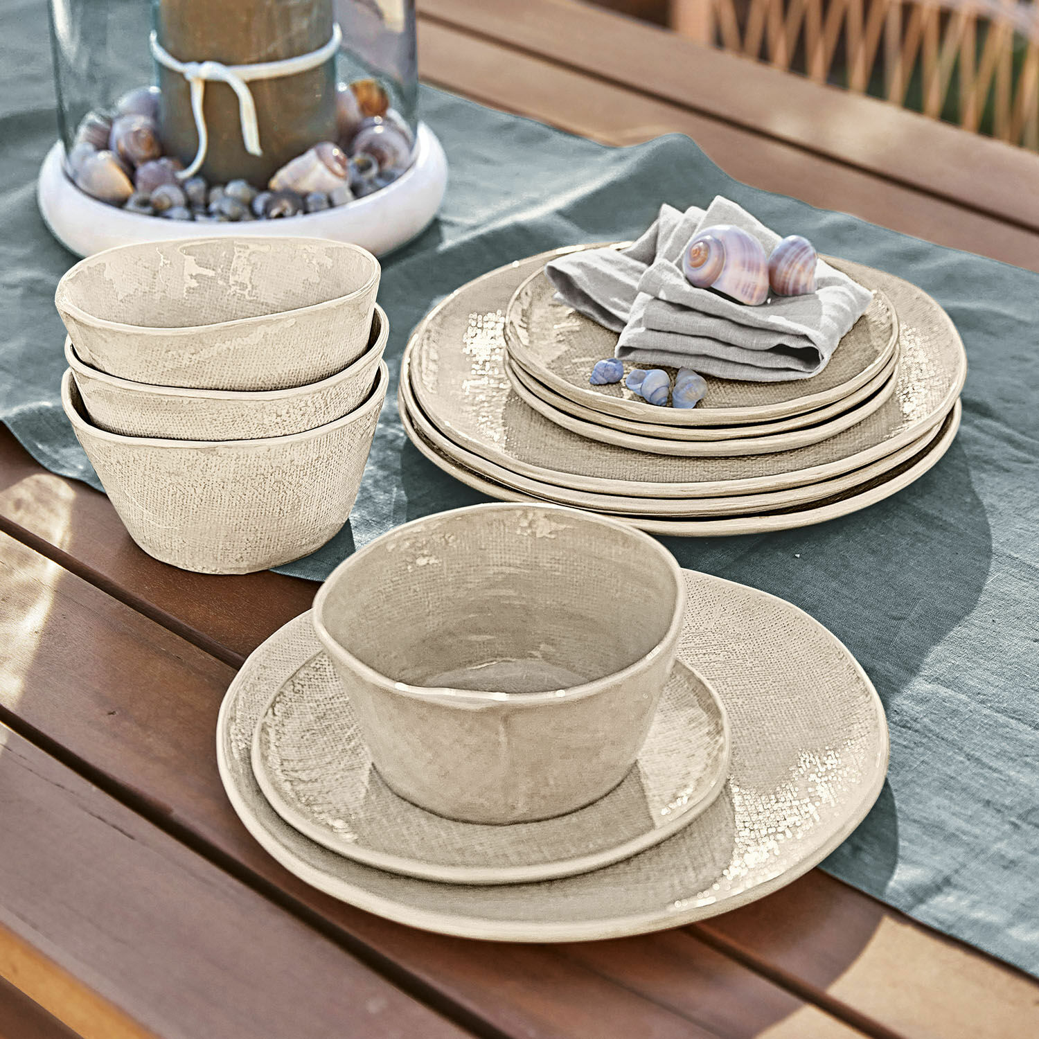 Geschirr 12er Set Luganville Beiges Keramik-Geschirrset auf Holztisch mit Muscheln und Leinentuch für Outdoor-Essen