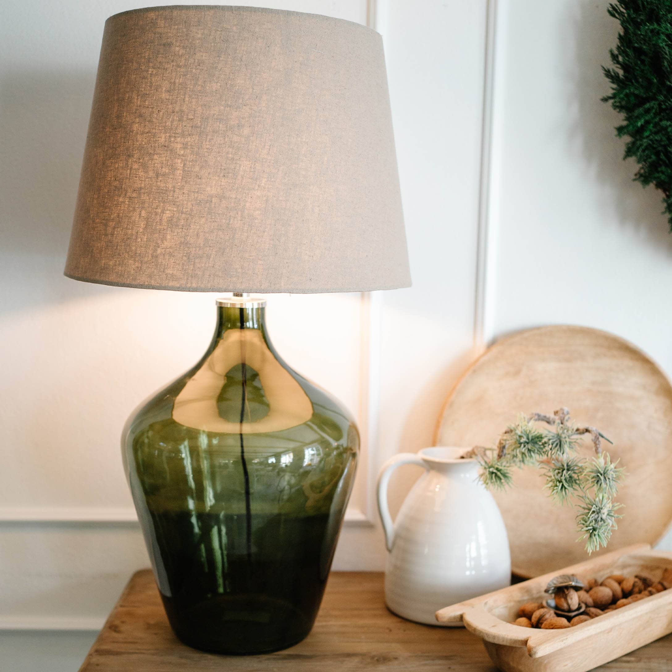 Tischlampe aus grünem Glas mit beigem Lampenschirm auf Holztisch mit Dekorationen