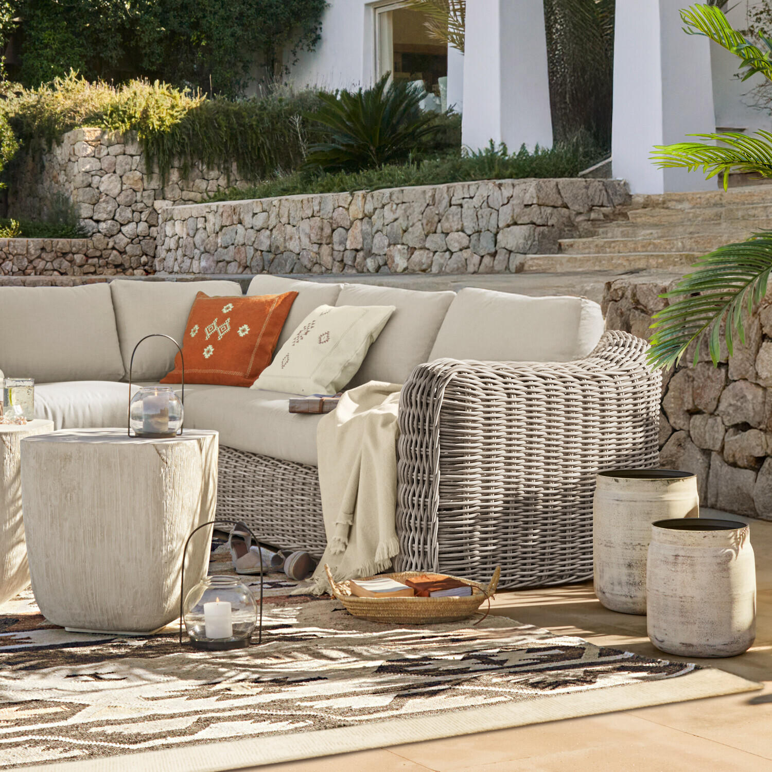 Sofa Eravinto Gartenmöbel-Set aus grauem Rattan mit beigen Polstern auf Terrasse mit Natursteinmauer