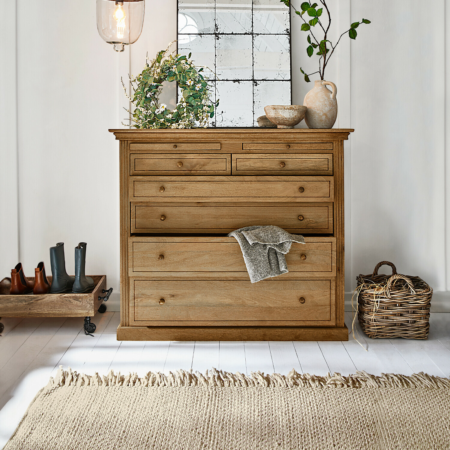 Holzkommode in Naturfarbe mit mehreren Schubladen, Dekorationen und hellem Teppich in einem hellen Raum