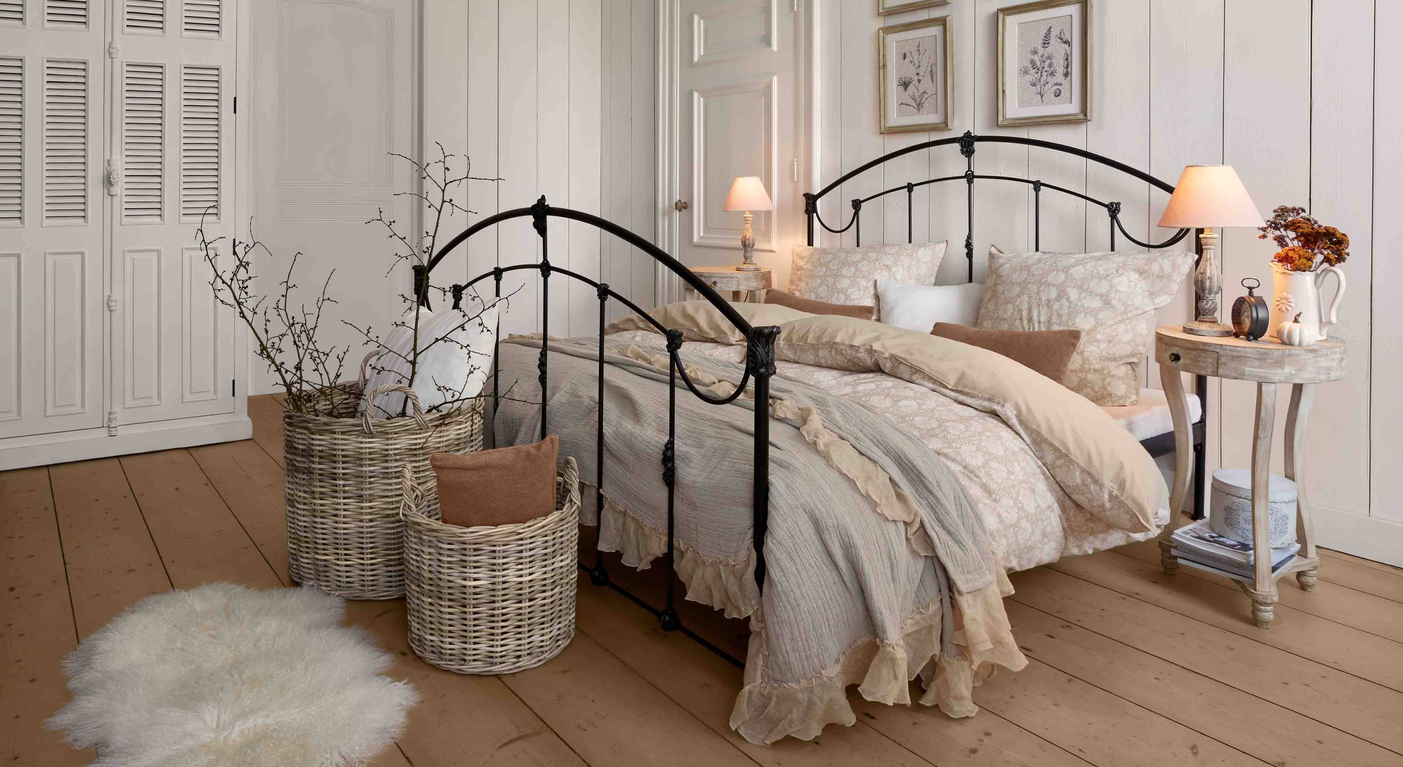 Schlafzimmer mit schwarzem Metallbett und beiger Vintage-Bettwäsche, Korb aus Weide und Nachttischlampe