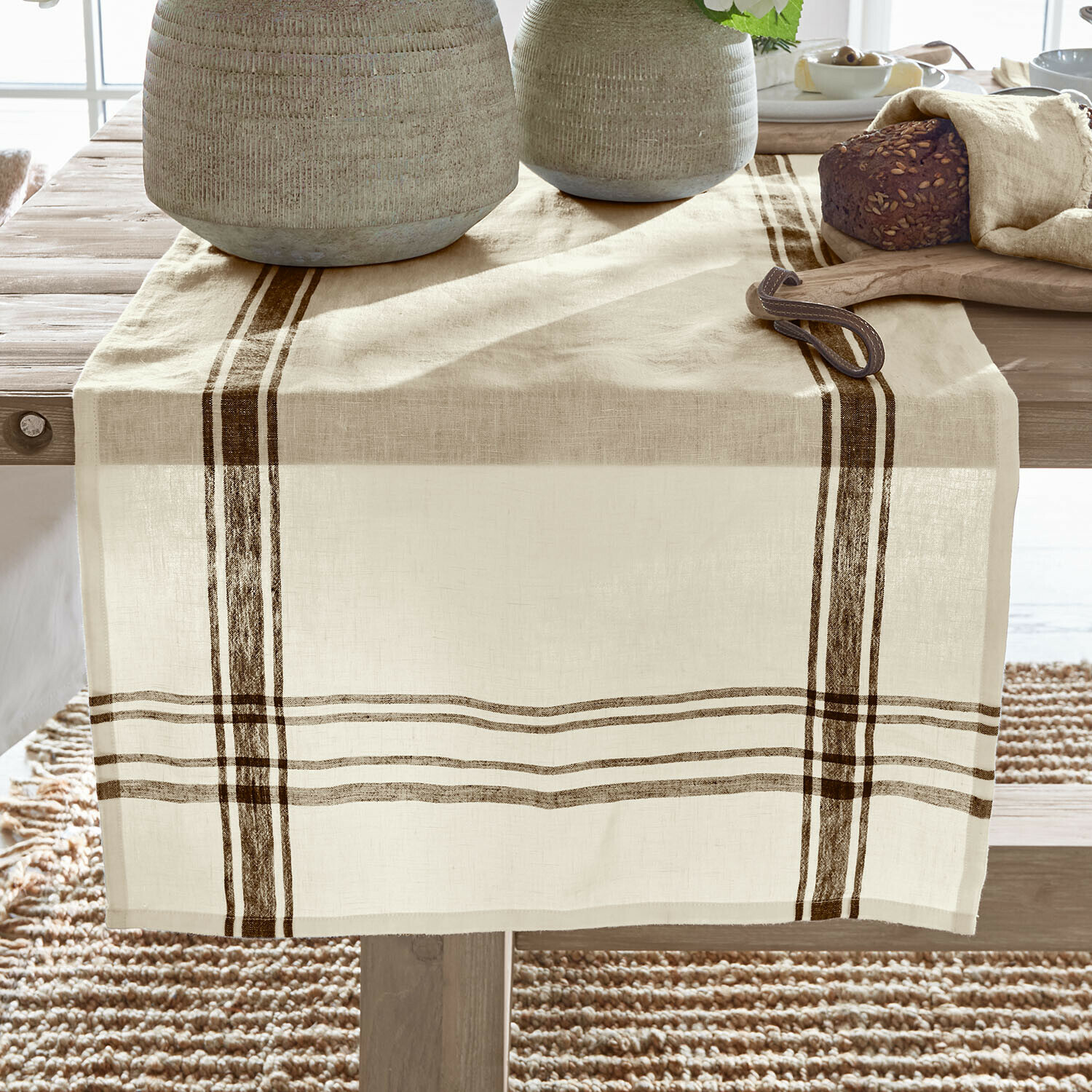 Beiger Leinen-Tischläufer mit braunen Streifen auf Holztisch, dekoriert mit Brot und Keramik