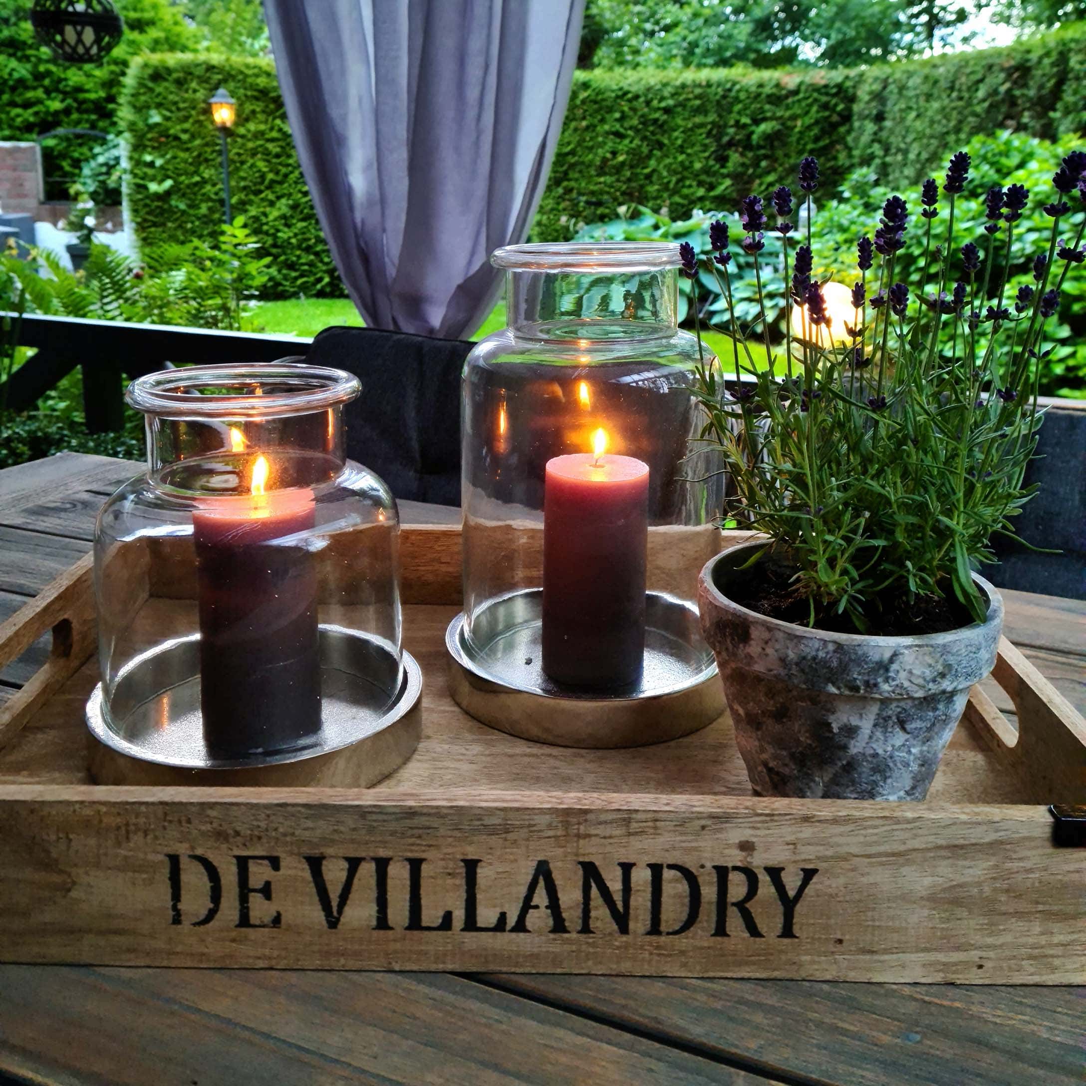Holztablett mit zwei Glaslaternen und einem Lavendeltopf auf Holztisch im Garten