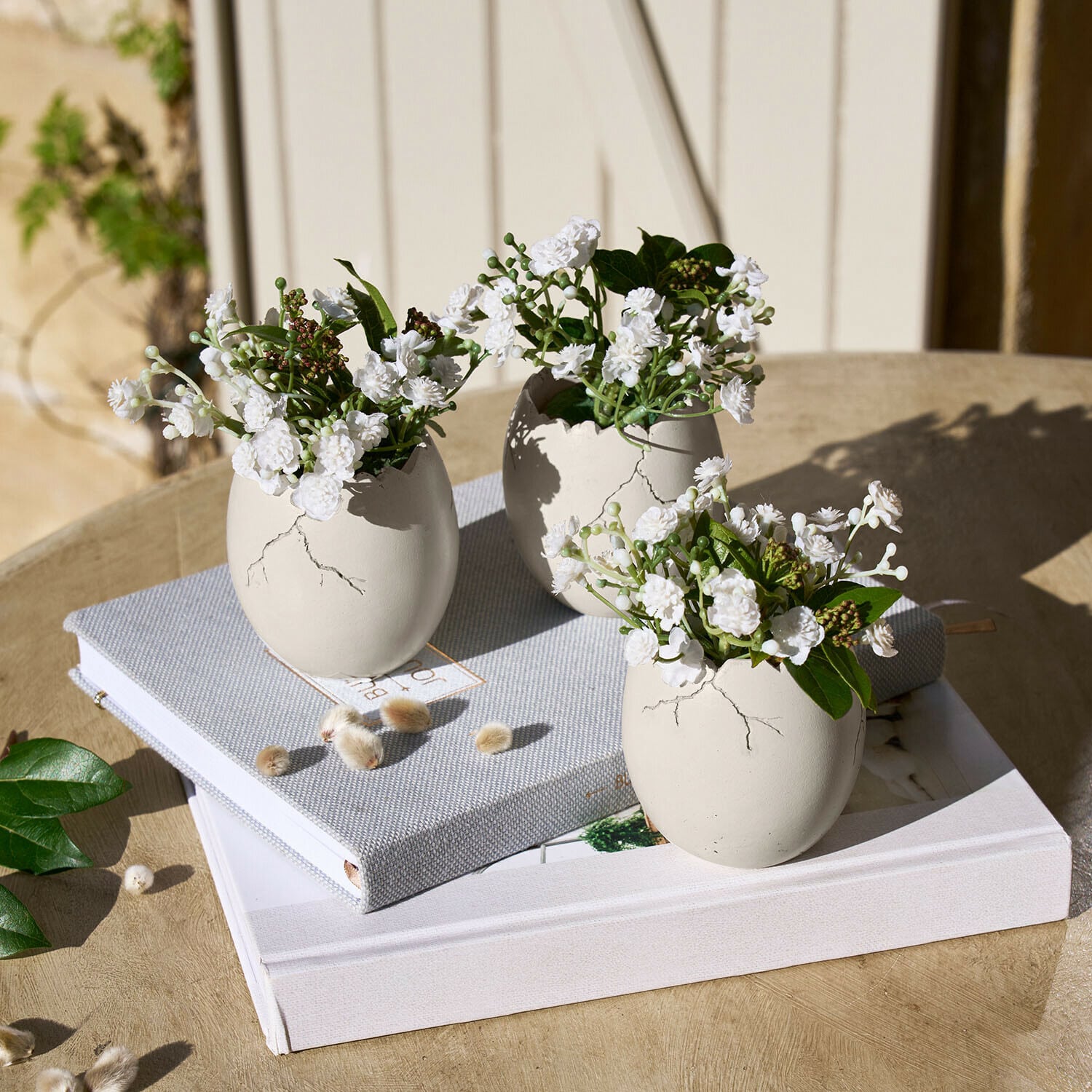 Deko-Ei 3er Set Waverlye Drei weiße Keramikvasen in Ei-Form mit weißen Blumen auf Holztisch mit Büchern